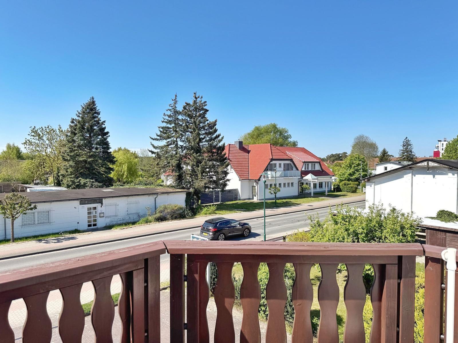 Blick vom Balkon auf Straße, Bäume und ein Haus mit rotem Dach.