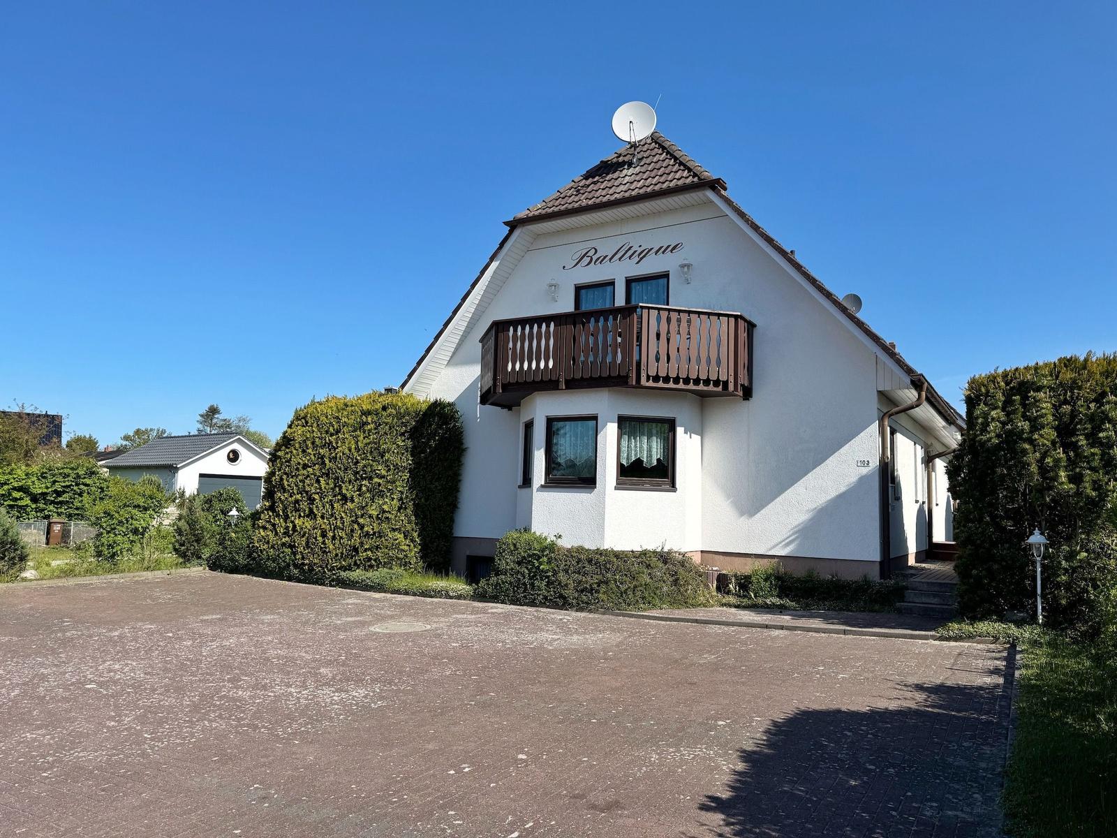 Weiße Villa mit Balkon und Satellitenschüssel unter blauem Himmel.