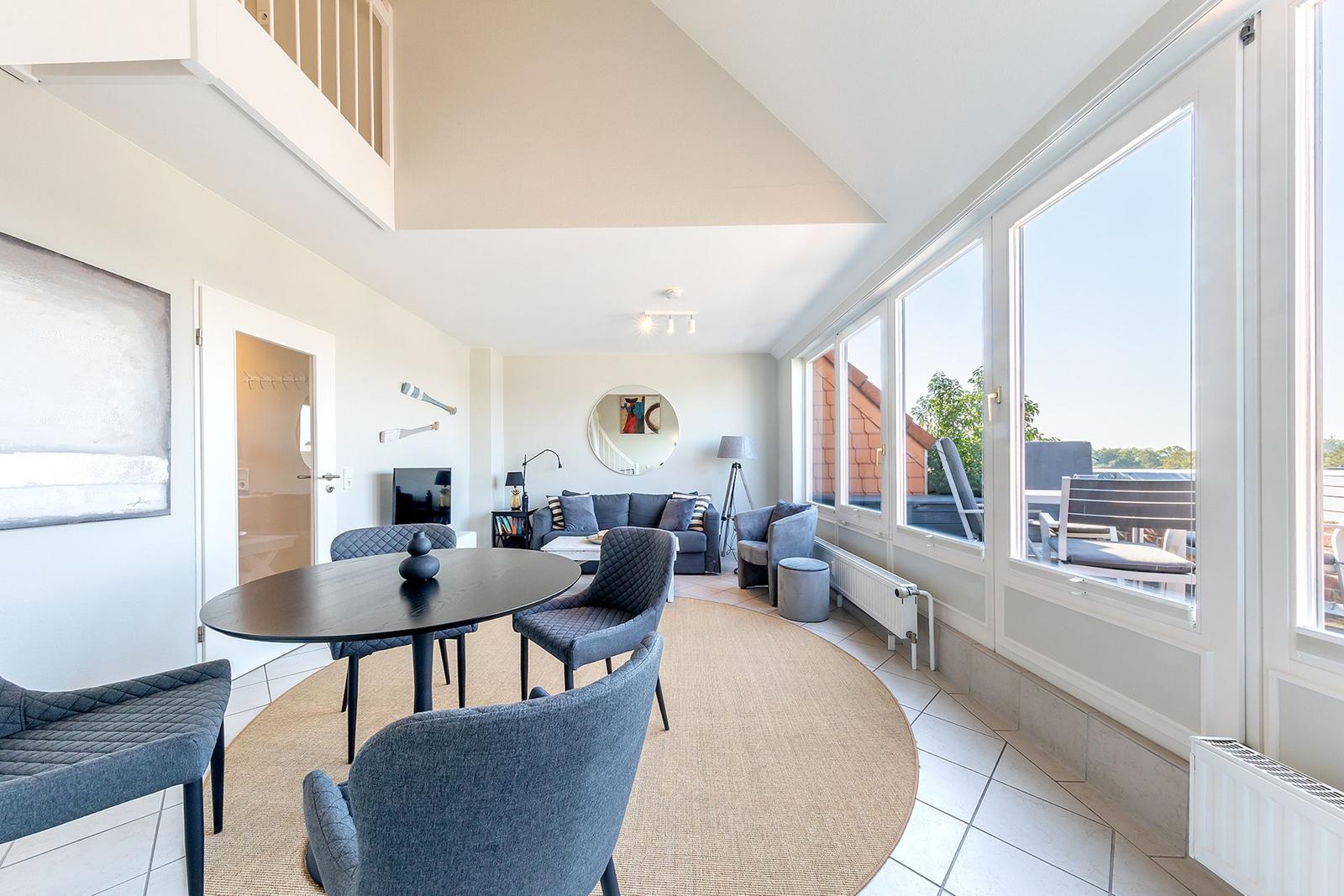 Essbereich mit Tisch und Stühlen. Wohnbereich mit Sofa und Blick auf Balkon.