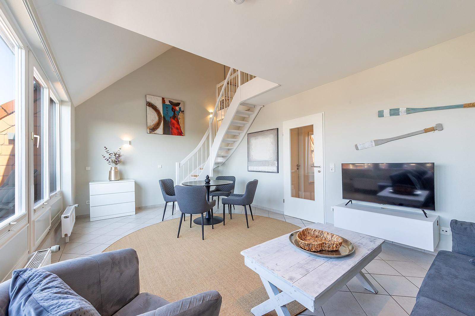 Wohn- und Essbereich mit Treppe und TV. Rundteppich, Sofa und Esstisch.