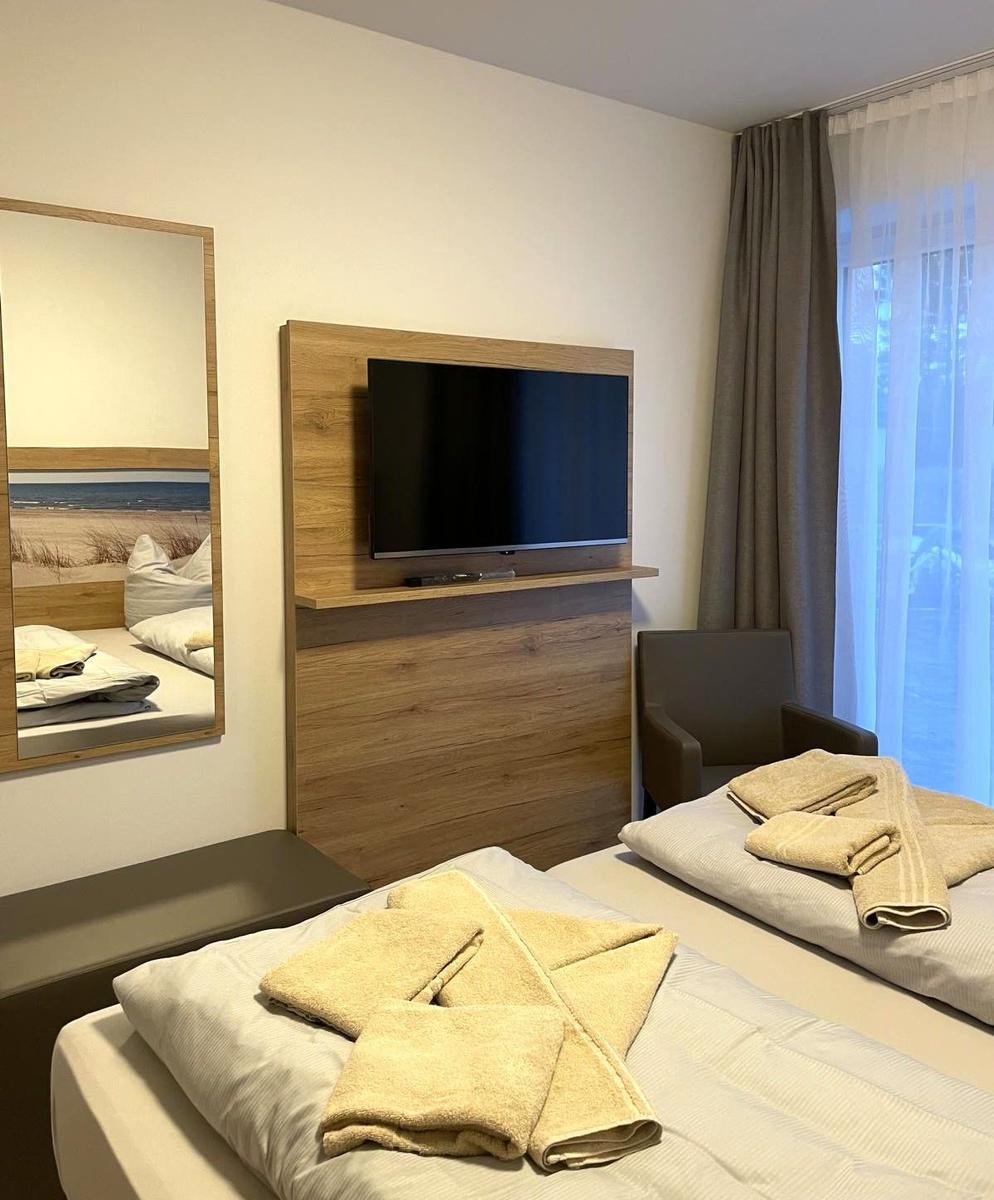 Zimmer mit Bett, Fernseher und Spiegel. Vorhang vor Fenster.