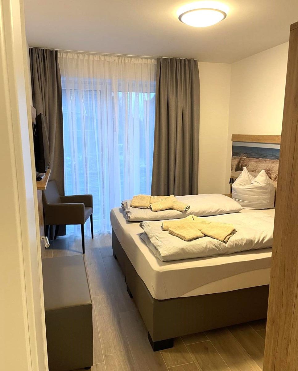 Schlafzimmer mit Doppelbett, TV und Fenster mit Vorhängen.