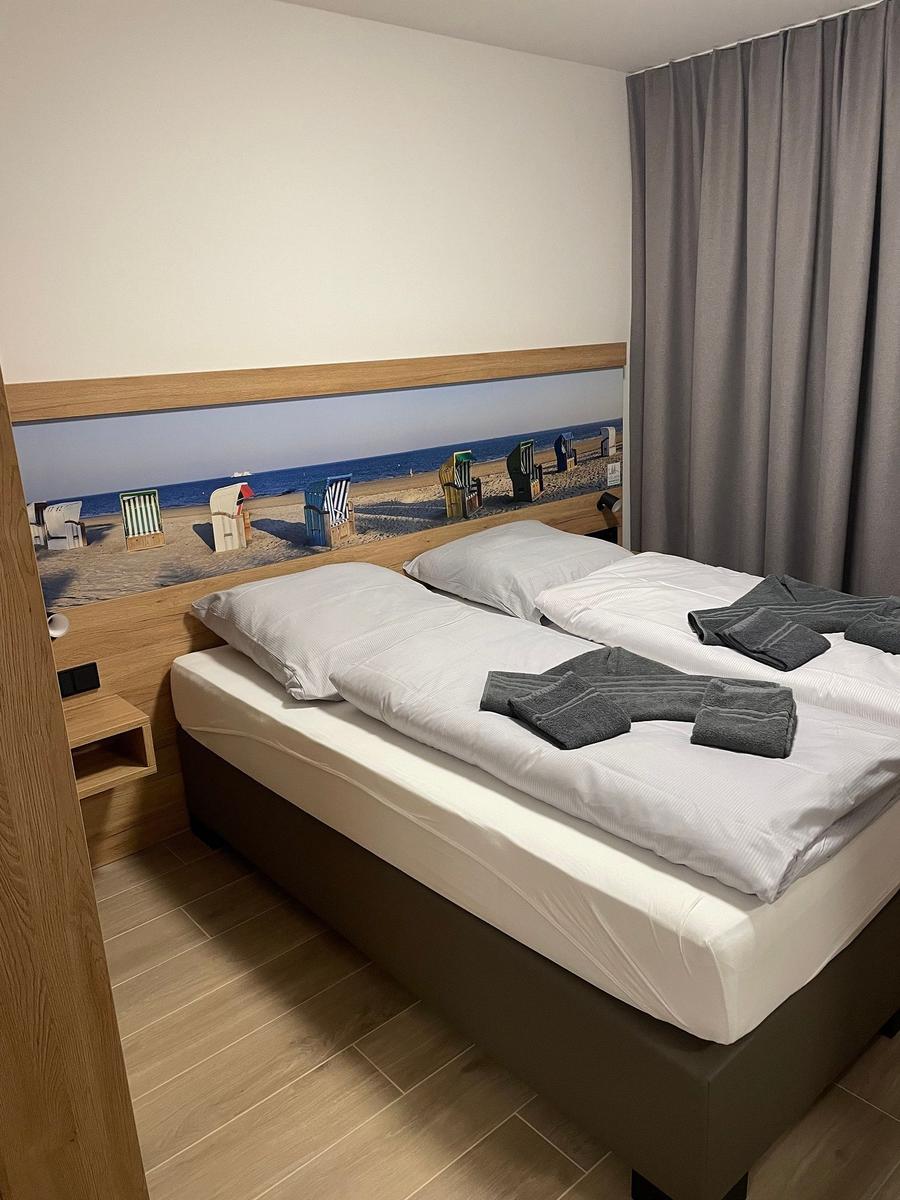 Doppelbett mit Strandmotiv an der Wand und grauen Vorhängen.