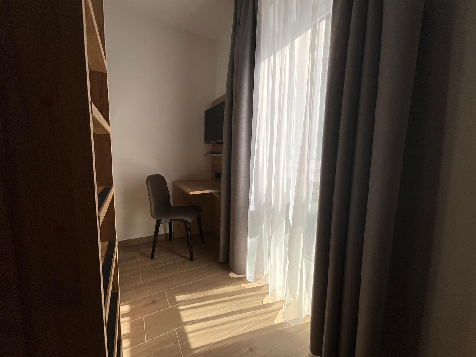 Schreibtisch mit Stuhl und TV unter Fenster mit Vorhängen.