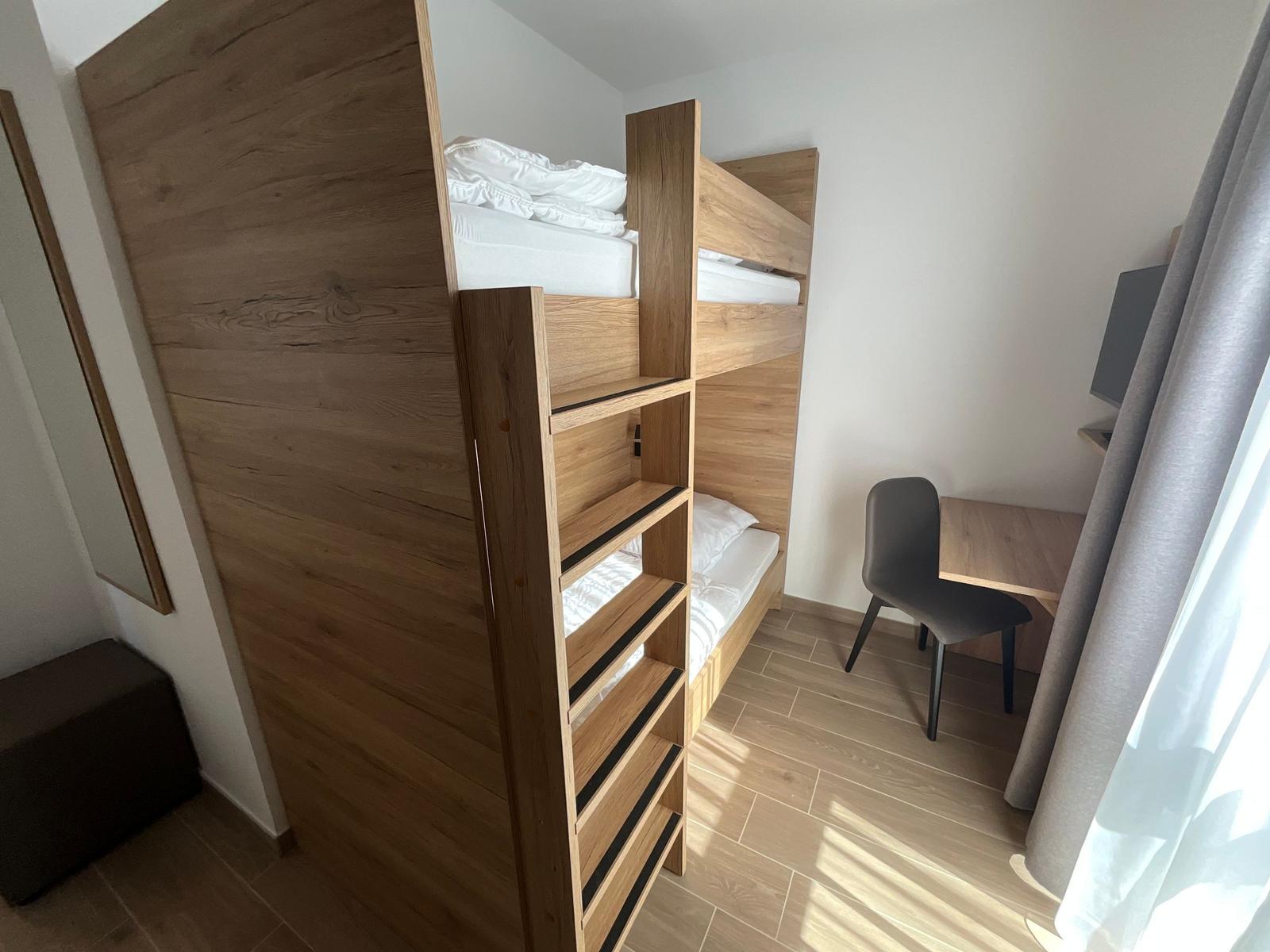 Zimmer mit Doppelstockbett, Schreibtisch und Stuhl.