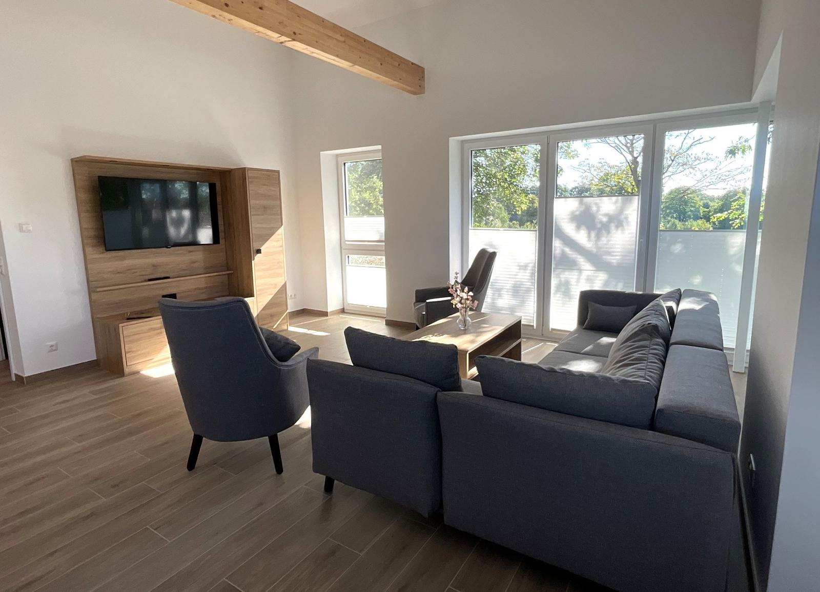 Wohnzimmer mit Sofa, Sessel und Fernseher an der Wand.