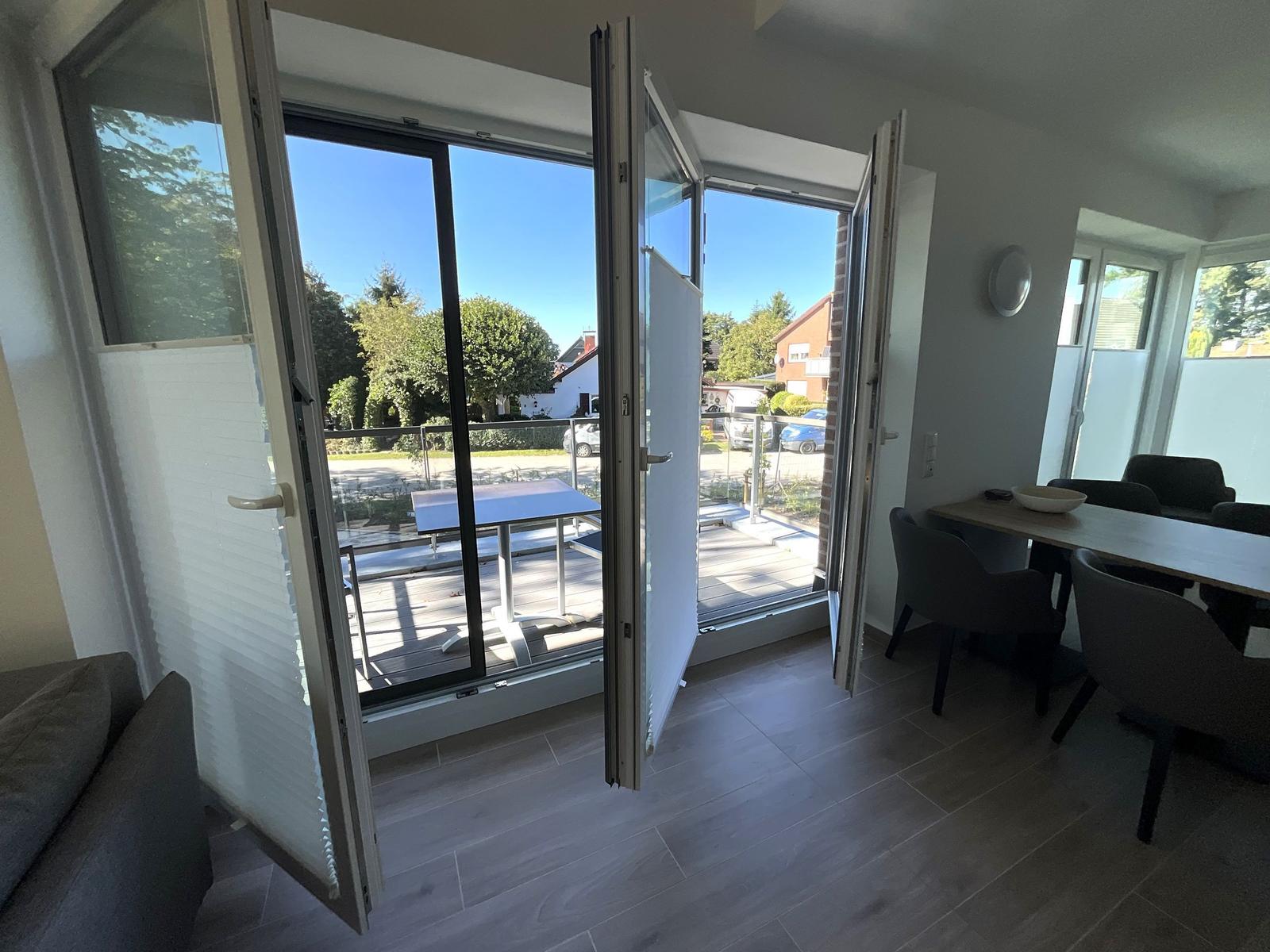 Offener Raum mit Essbereich und Terrasse. Große Fenster und Türen zur Außenterrasse.