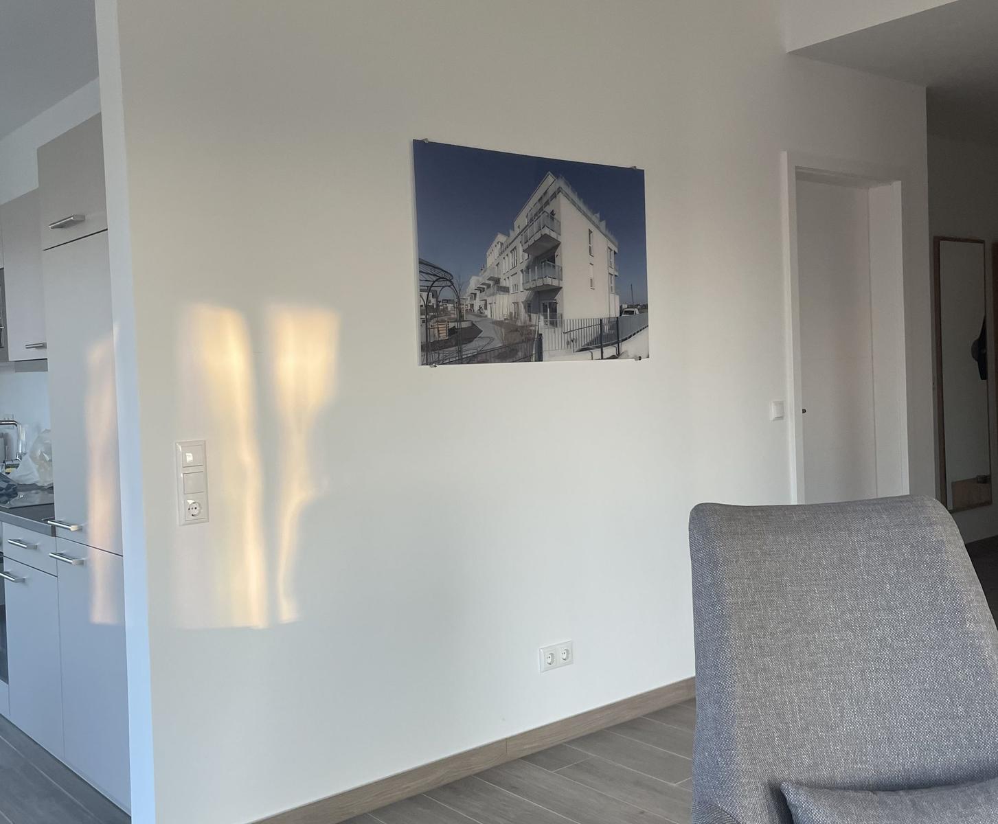 Wohnzimmer mit grauem Sessel und Wandbild. Küchenbereich links sichtbar.