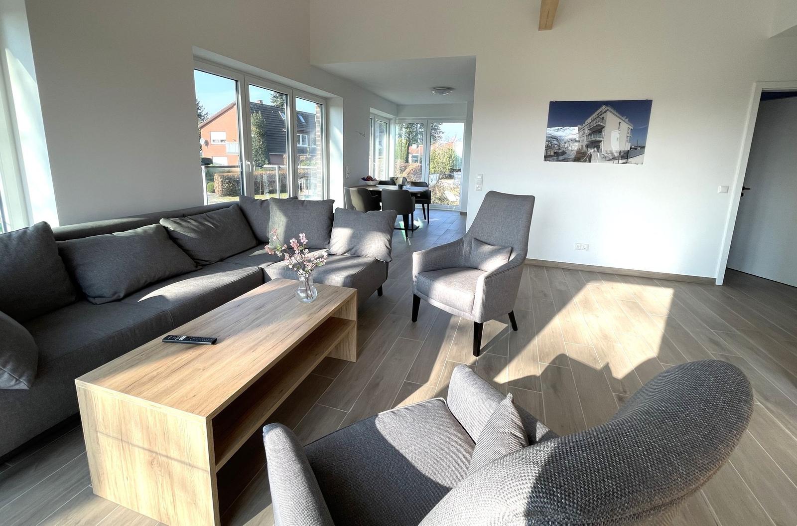 Wohnzimmer mit Sofa, Sessel und Holztisch. Durchgang zum Essbereich mit Tisch und Stühlen.