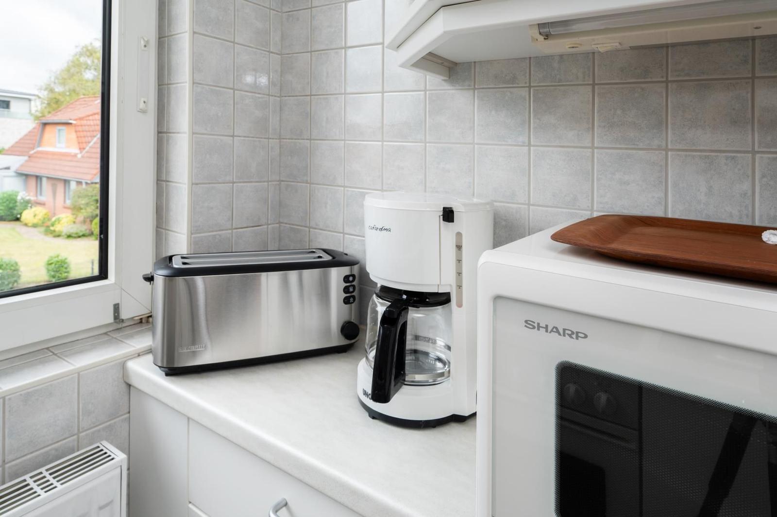 Küchenzeile mit Toaster, Kaffeemaschine und Mikrowelle. Fenster mit Blick auf Garten.