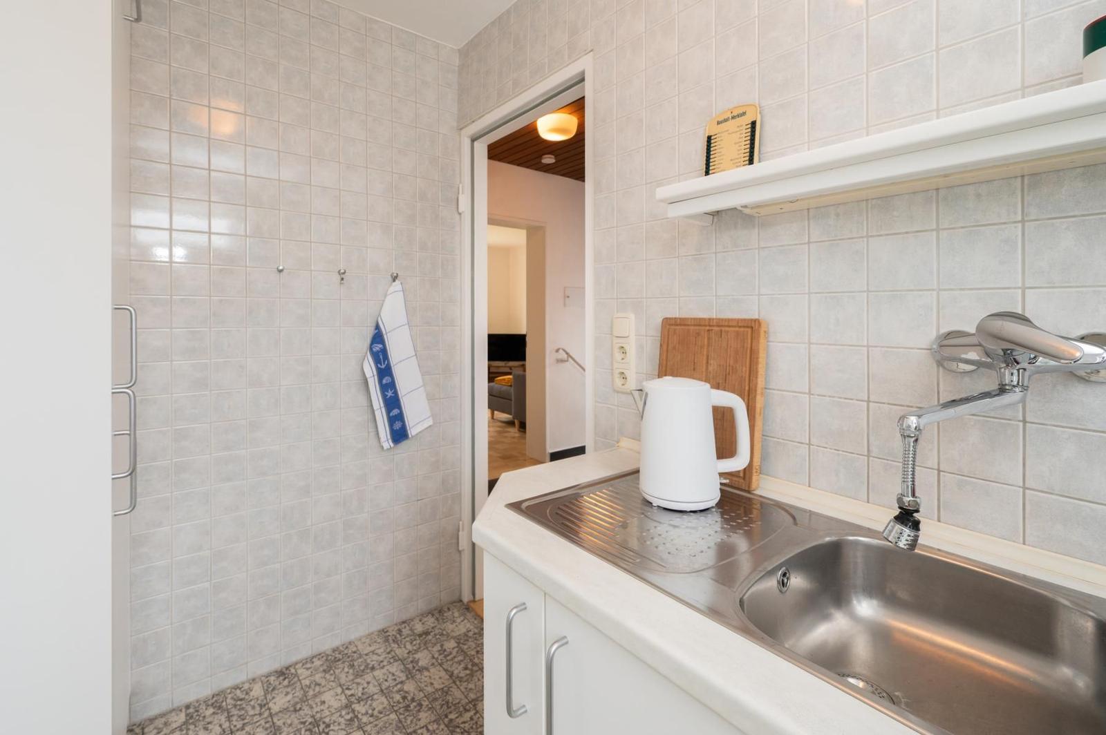 Küche mit Spüle, Wasserkocher und Küchenbrett. Hintergrund: Wohnbereich.