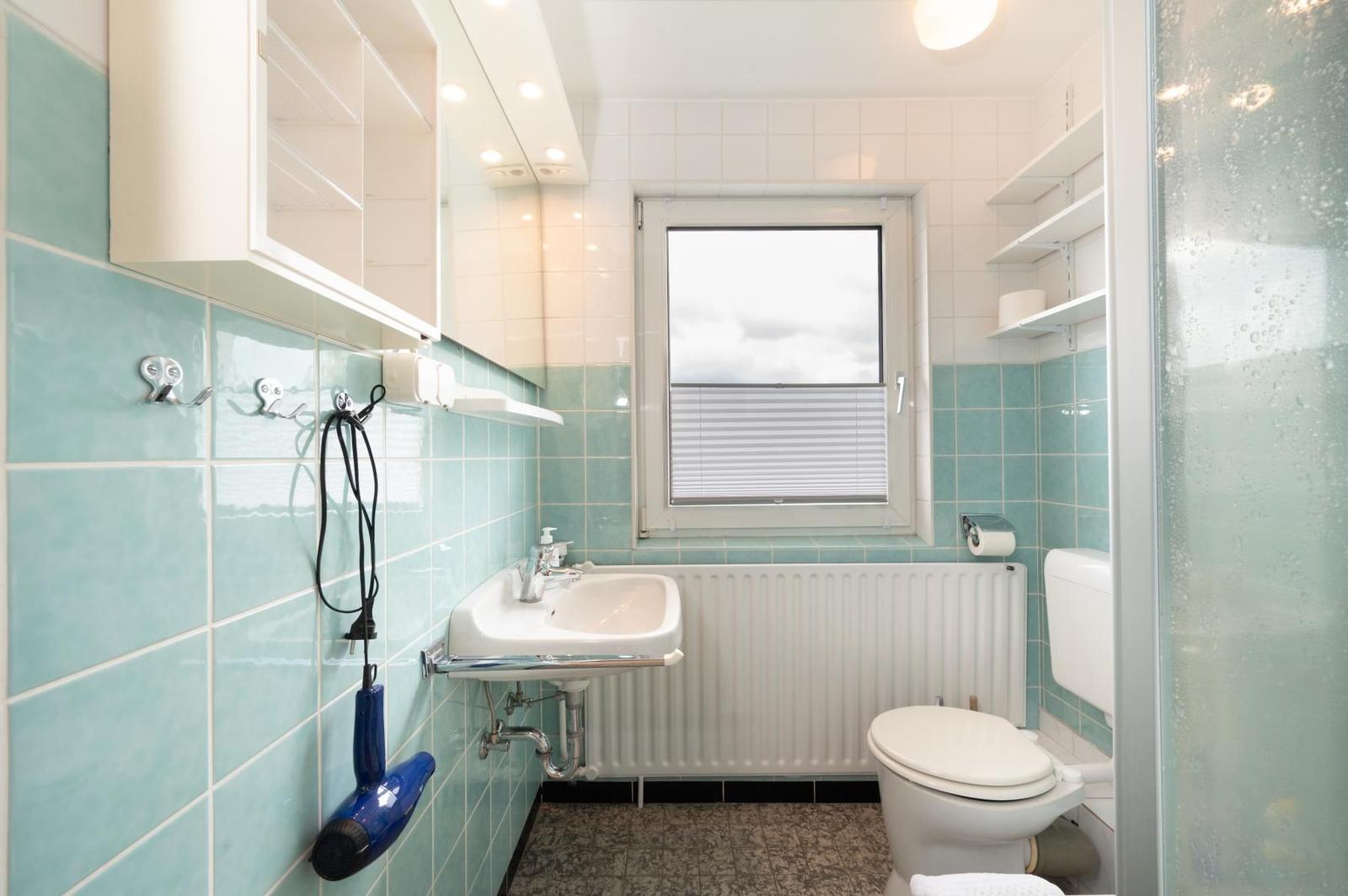 Badezimmer mit Waschbecken, Toilette und Dusche. Wandfliesen in Türkis und Weiß.