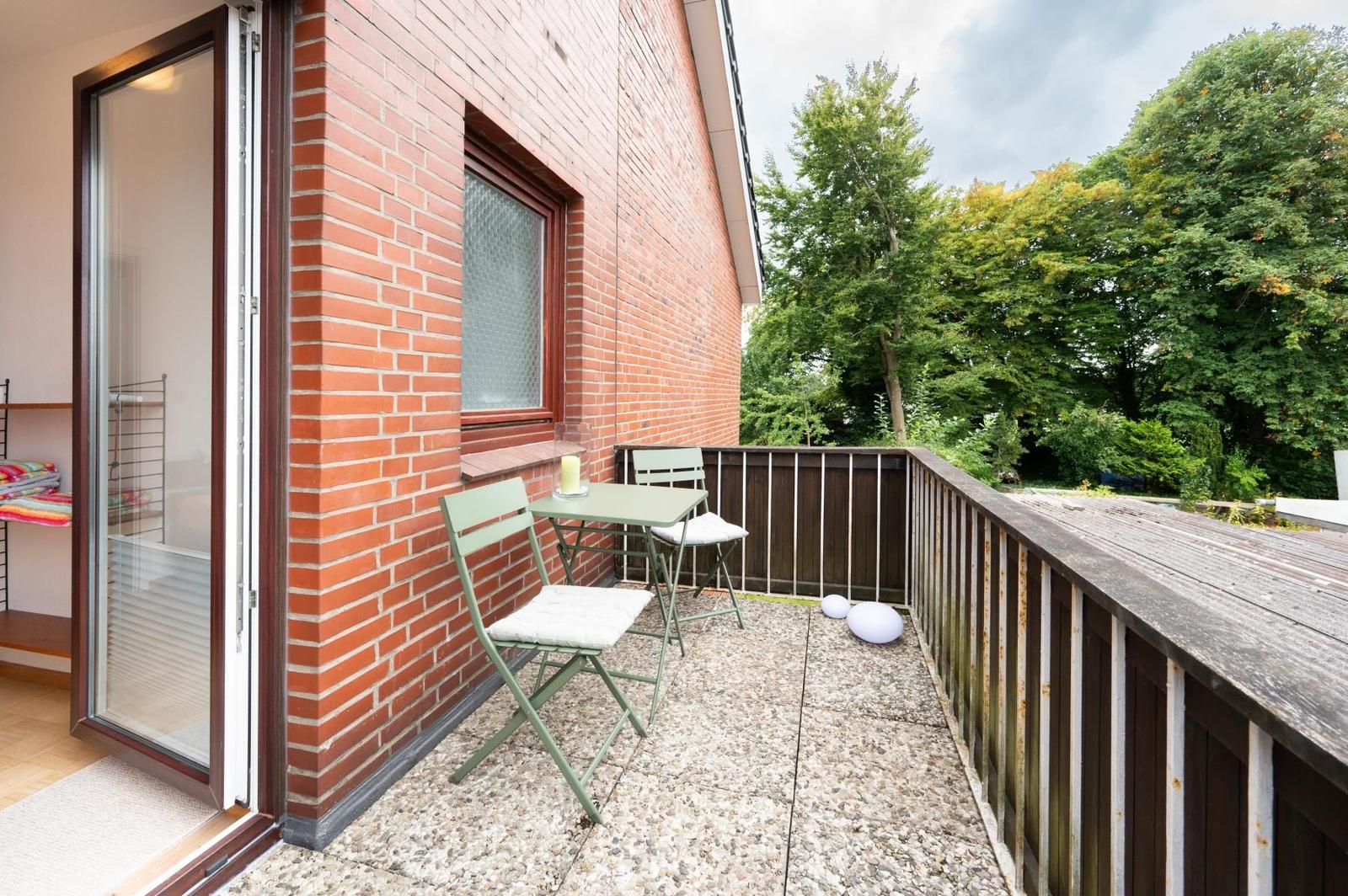 Terrasse mit Tisch, zwei Stühlen und Blick auf grüne Bäume.