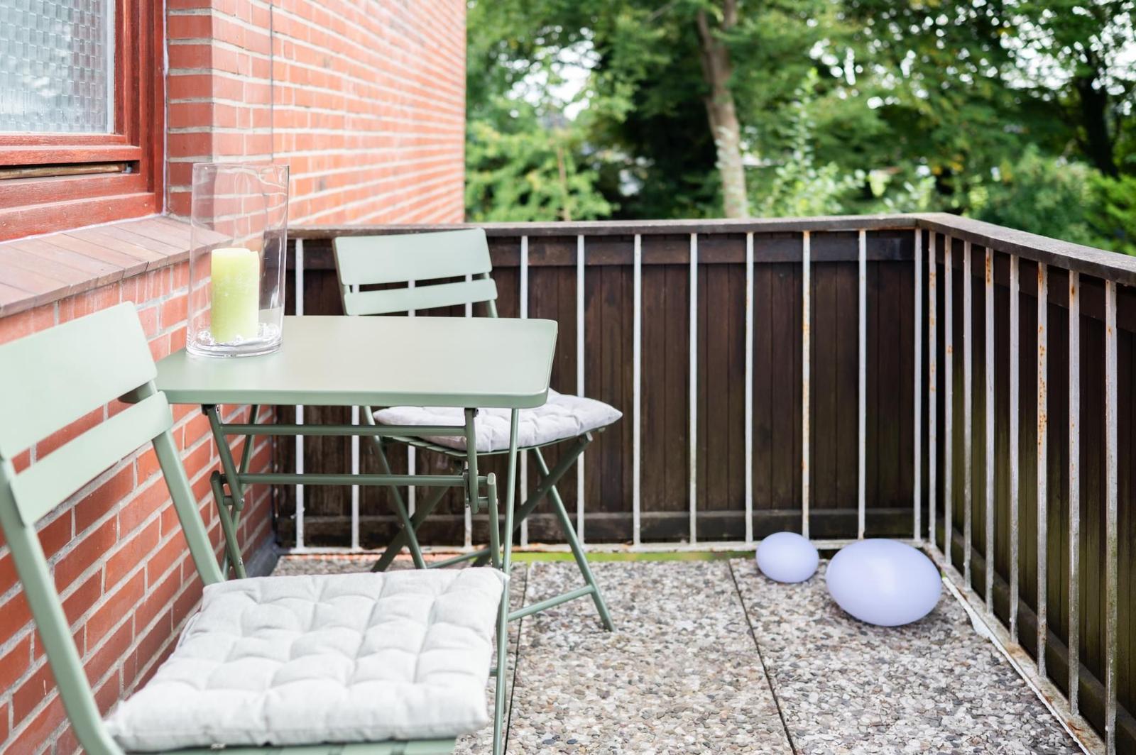 Terrasse mit Tisch, zwei Stühlen und zwei Luftballons. Hintergrund: Holzgeländer und grüne Bäume.