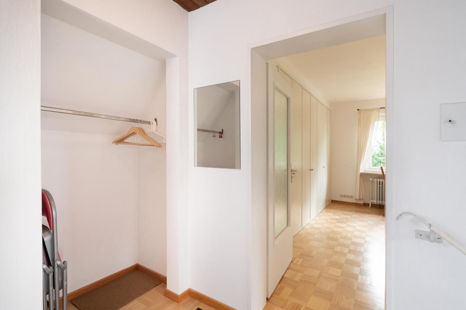 Flur mit Kleiderschrank, Spiegel und Tür zu einem Zimmer mit Holzboden.
