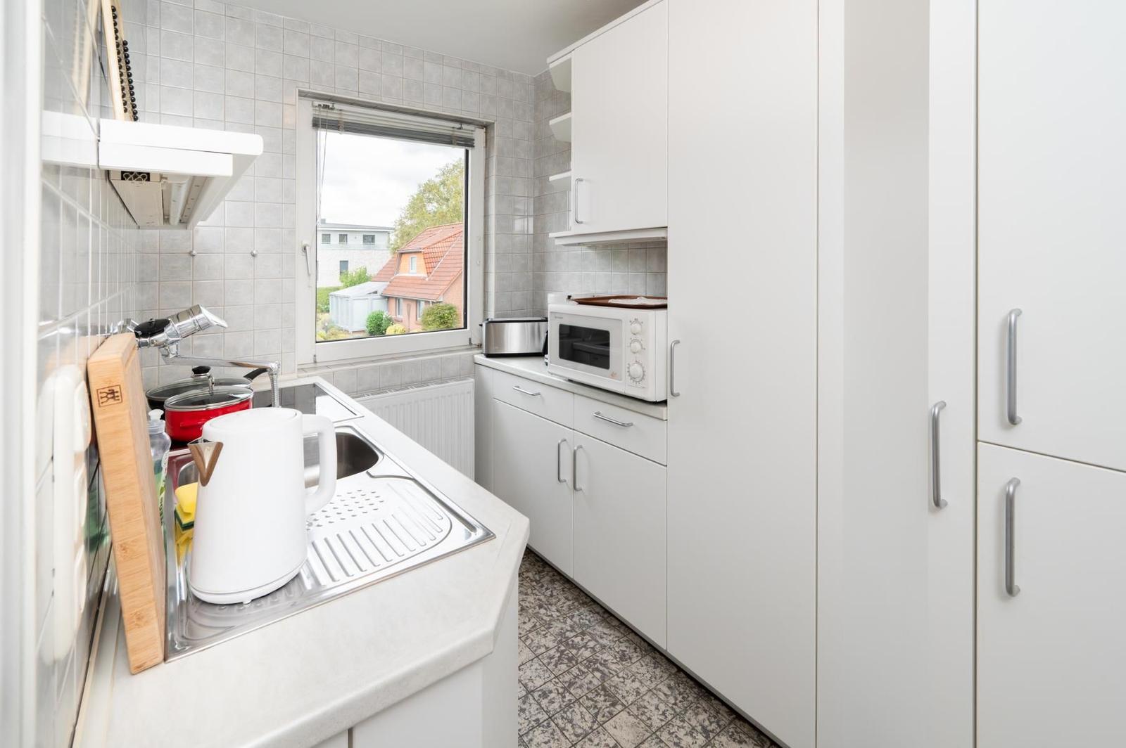 Küche mit weißen Schränken, Herd und Fensterblick.