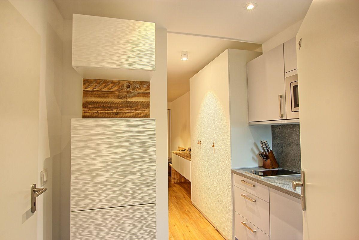 Küche mit weißen Schränken und Holzakzentwand. Durchgang zu Wohnbereich mit Holzboden.