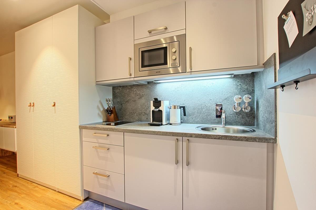 Küche mit weißen Schränken, Edelstahlspüle und Mikrowelle.