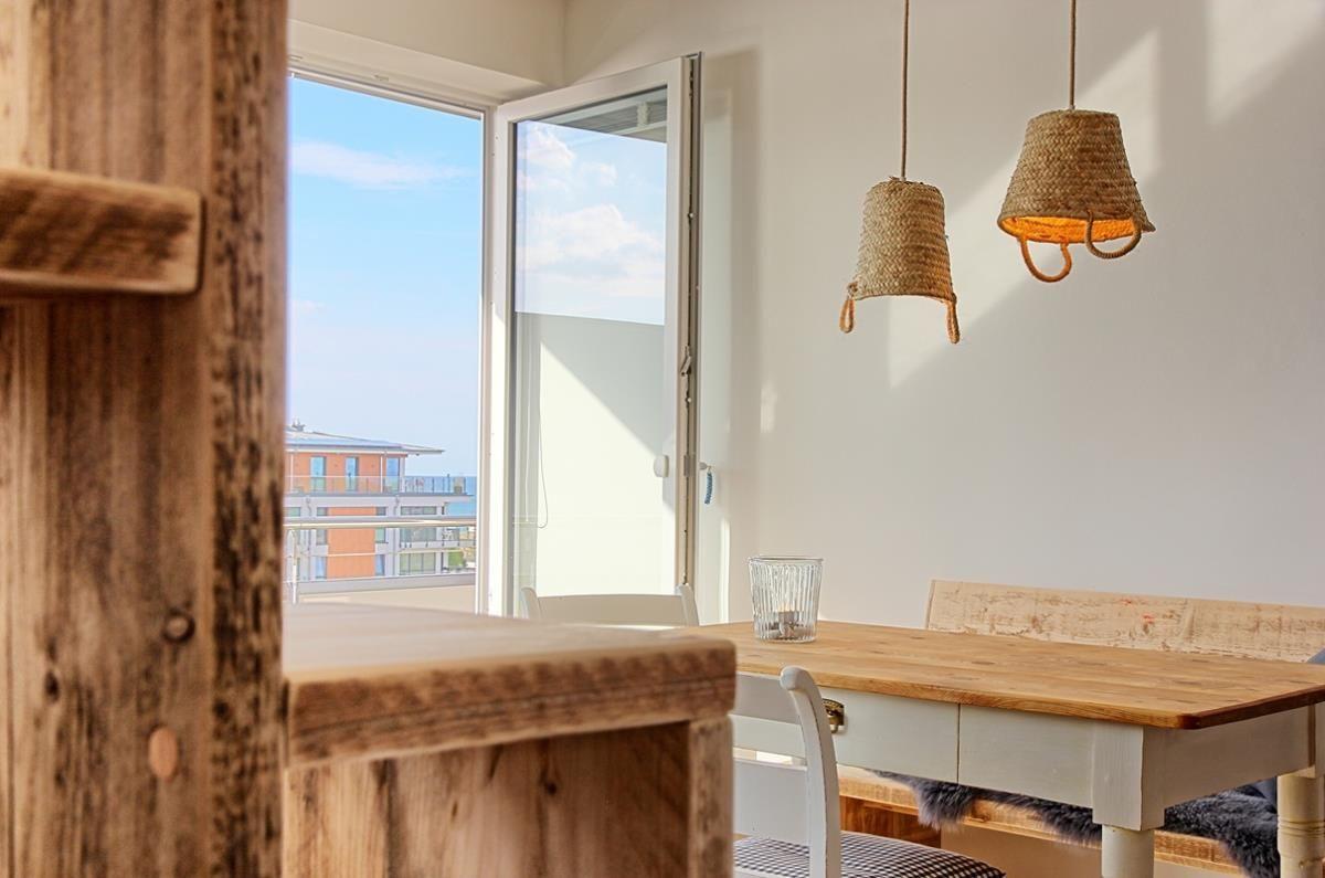 Essbereich mit Holztisch, Bänken und Hängelampen. Blick auf Balkon mit Stadtblick.