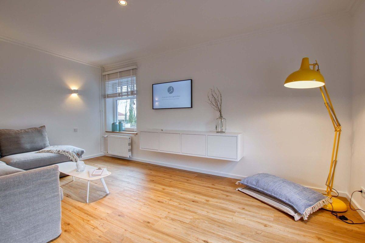 Wohnzimmer mit Sofa, Fernseher und gelber Stehlampe.