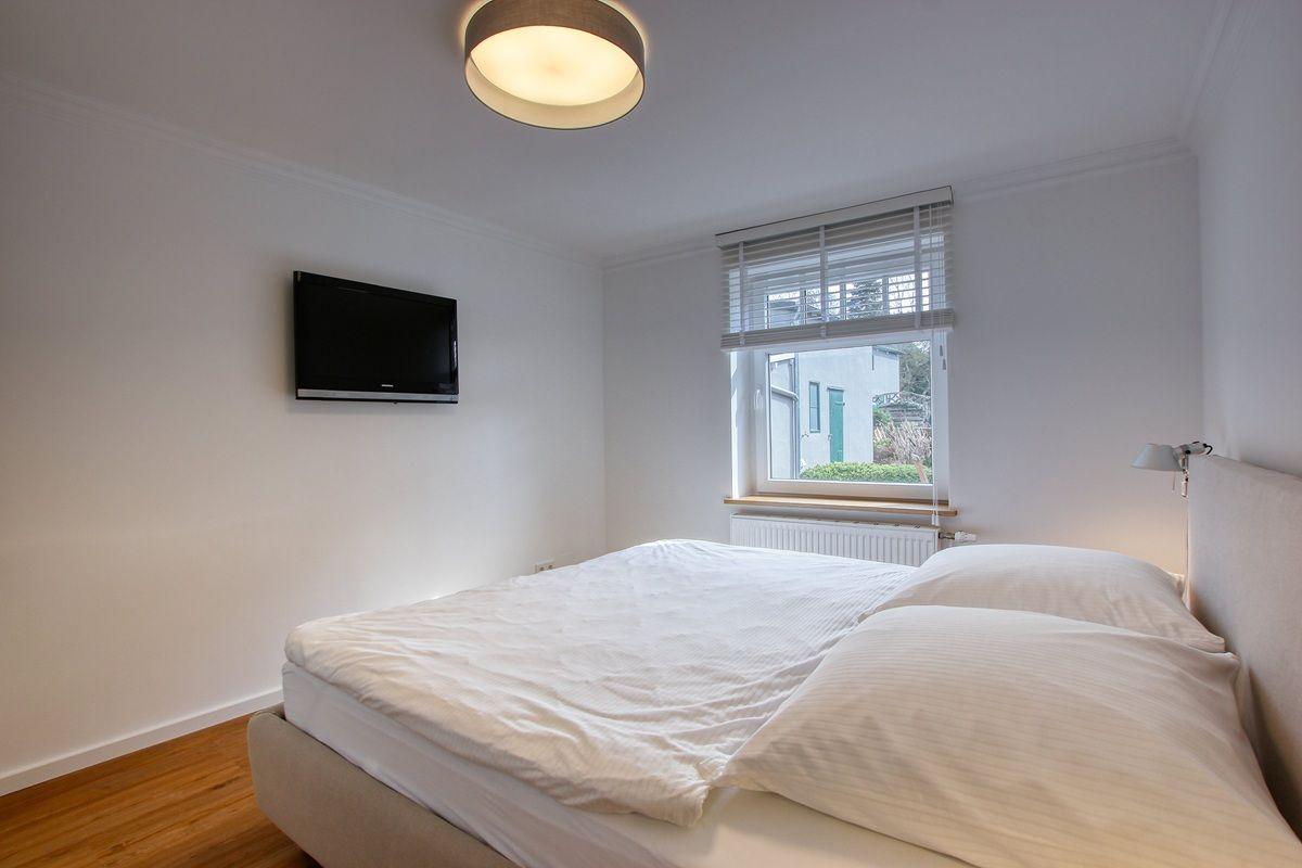 Schlafzimmer mit Bett, Fenster und Wandfernseher.