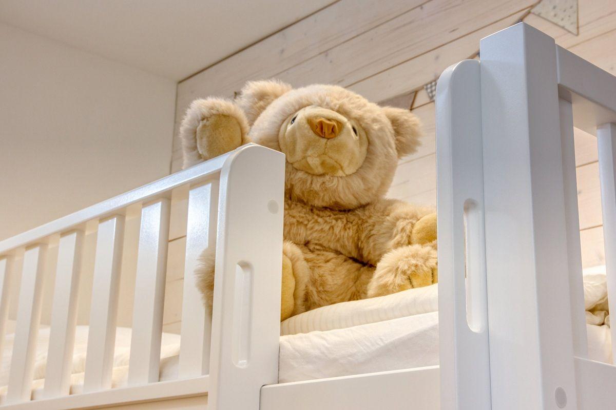 Ein weißes Kinderbett mit einem großen Teddybären darauf.