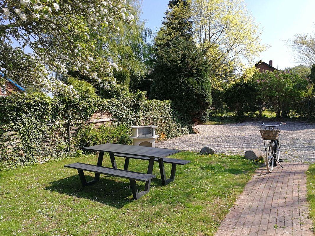 Garten mit Picknicktisch, Grill und Fahrrad auf Kiesweg.