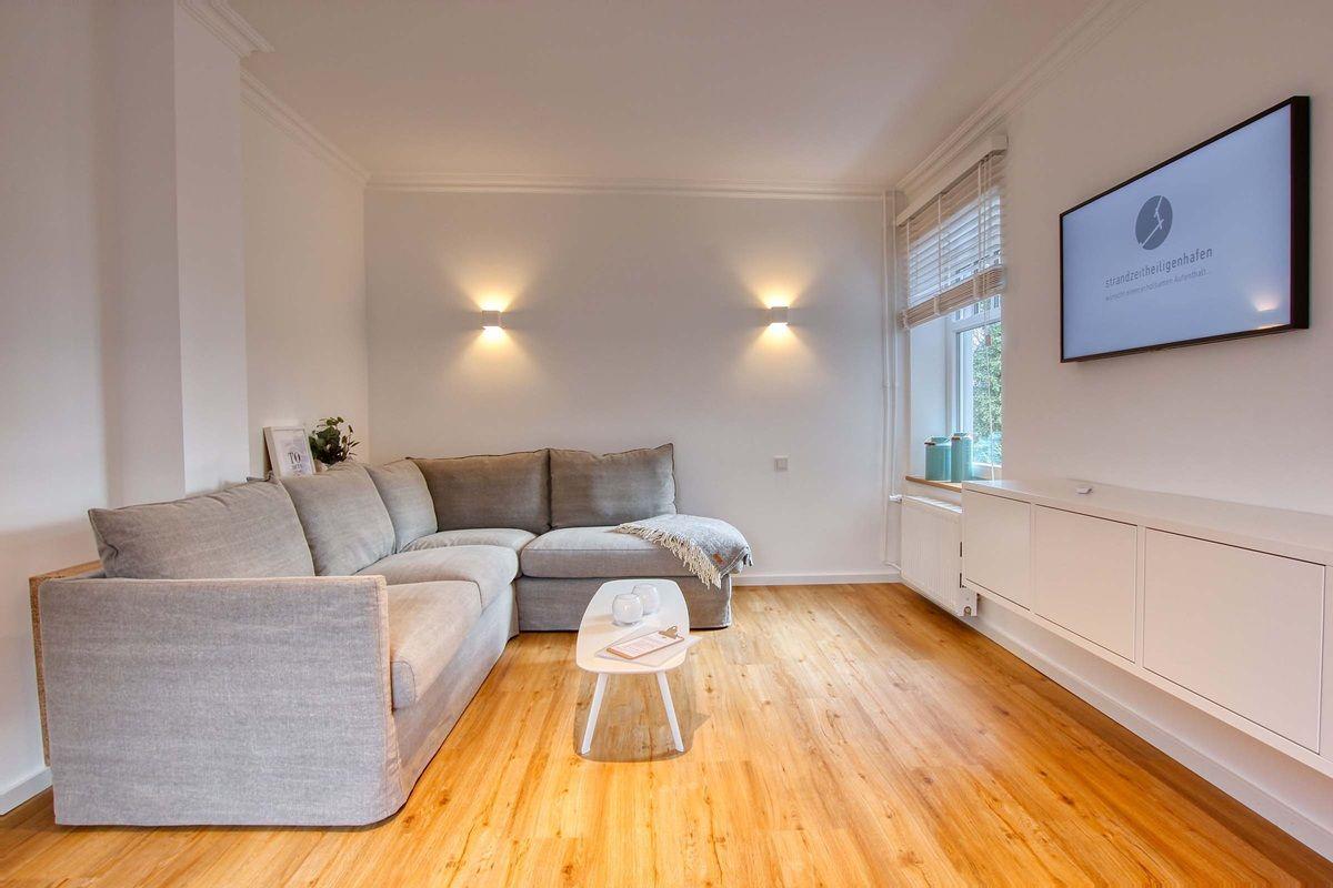 Wohnzimmer mit grauem Sofa, Holzboden und Wandfernseher.