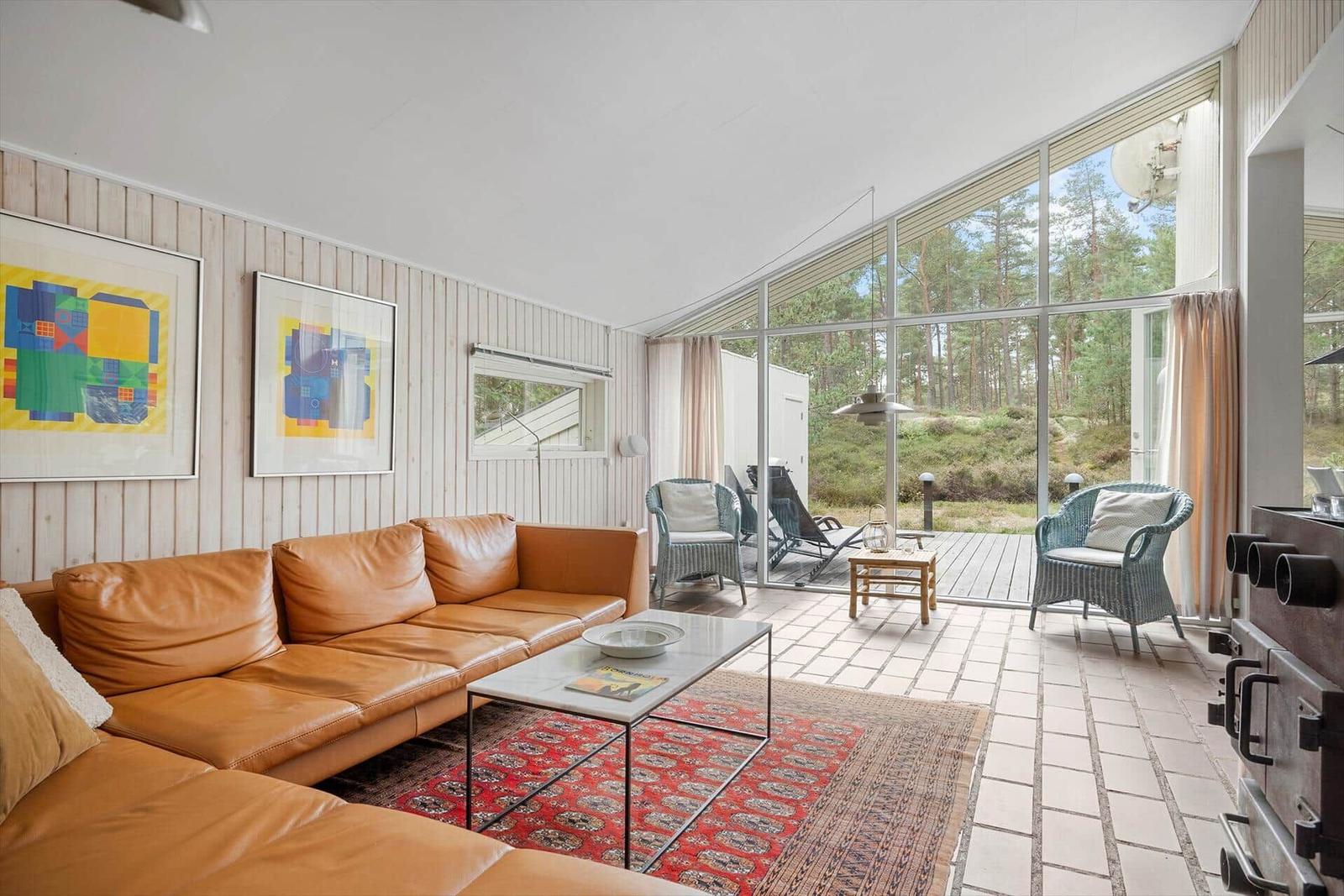 Wohnzimmer mit braunem Ledersofa, Glasfront und Blick auf Wald.