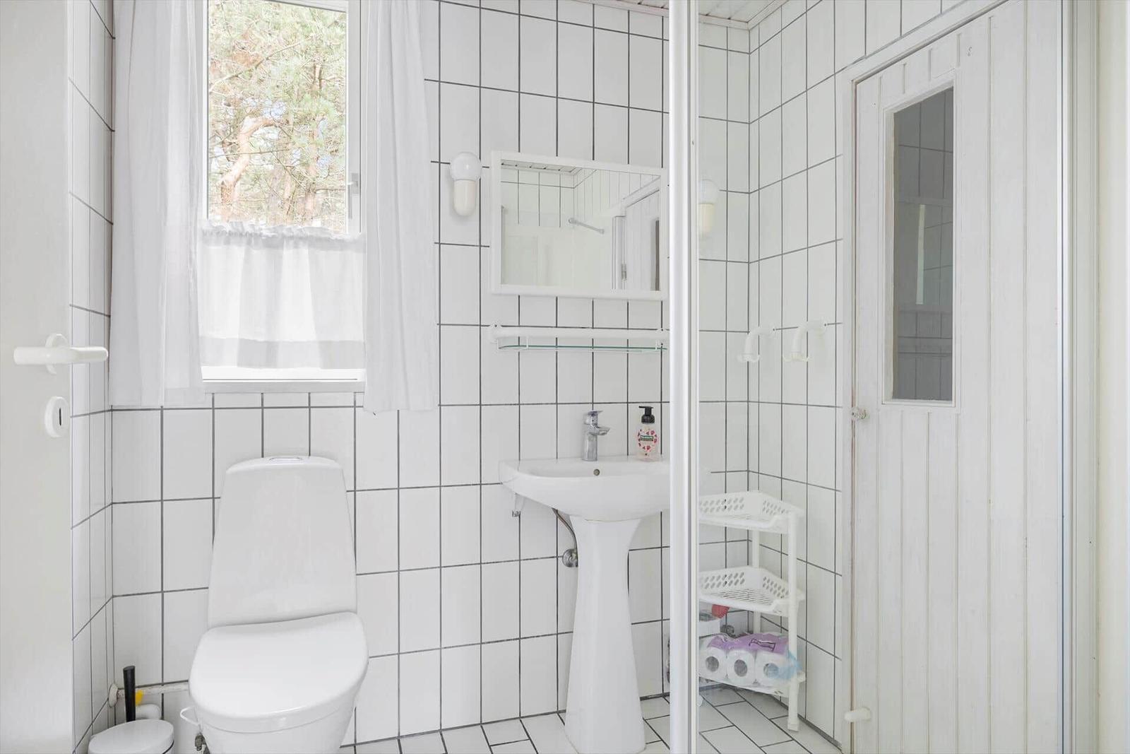 Badezimmer mit Toilette, Waschbecken und Dusche. Fenster mit weißen Vorhängen.