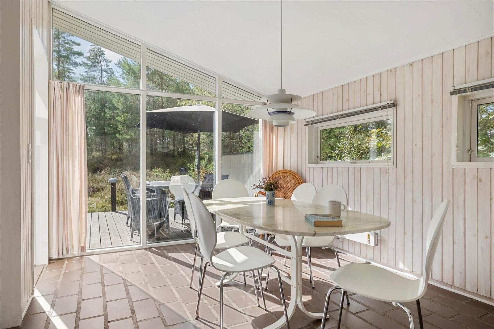 Esszimmer mit weißem Tisch und Stühlen, Holzwand und großem Fenster zum Garten.