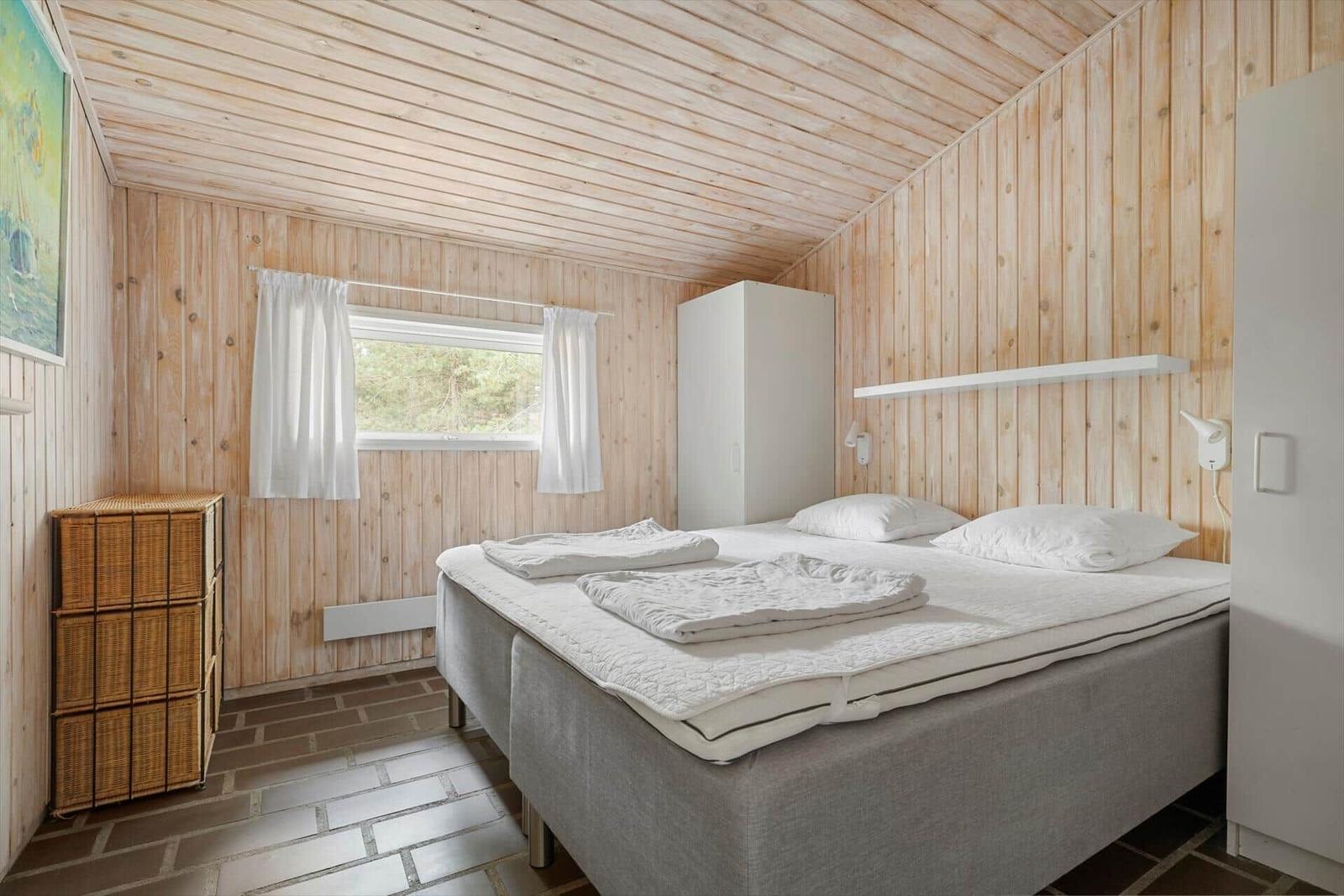 Schlafzimmer mit Holzwänden, Bett, Fenster und Schrank.