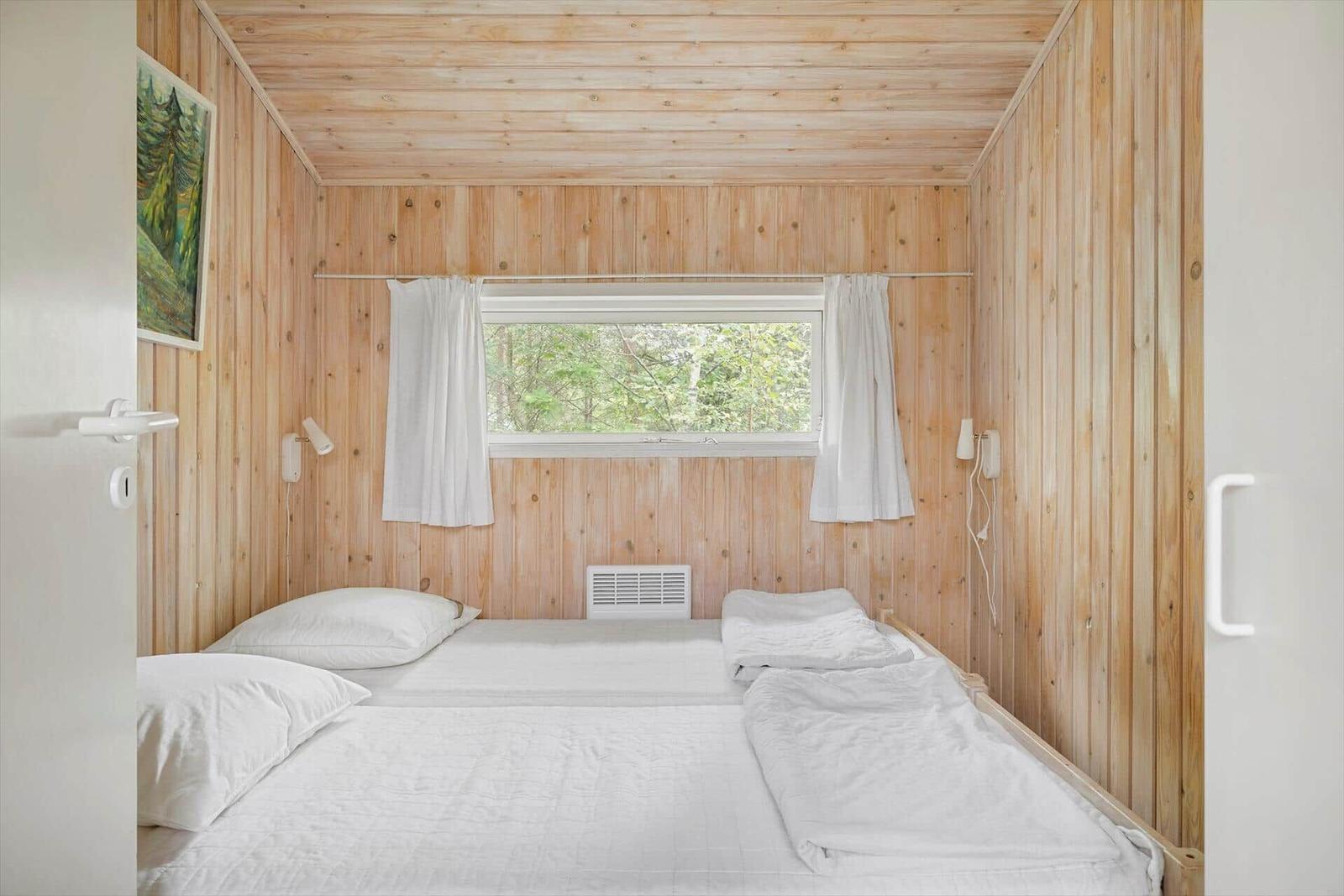Schlafzimmer mit Holzwand, Fenster und Bett mit weißen Laken.