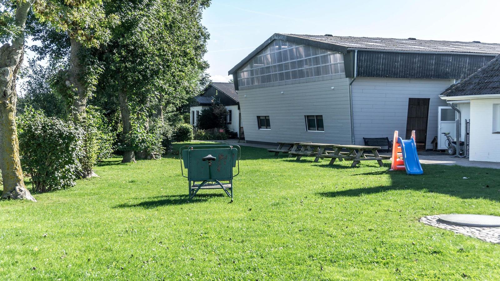 Grüner Garten mit Picknicktisch, Rutsche und grünem Kinderkarussell vor einem Gebäude.