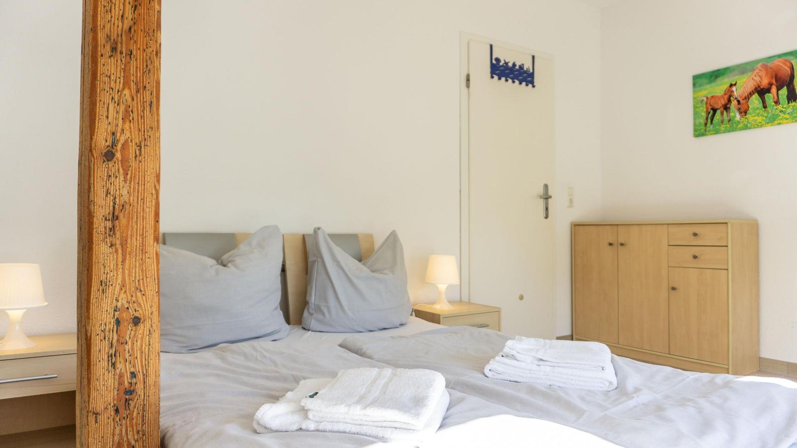 Ein Schlafzimmer mit Bett, Nachttischen und Schrank. An der Wand hängt ein Bild mit Pferden.