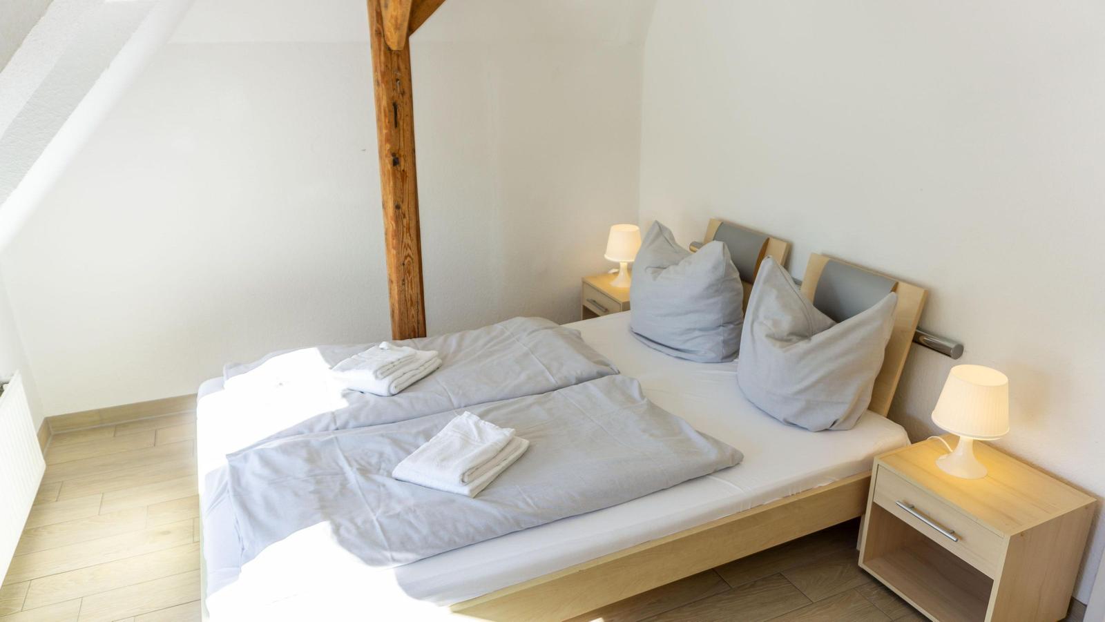 Ein Schlafzimmer mit Doppelbett, zwei Nachttischen und einem Holzbalken.