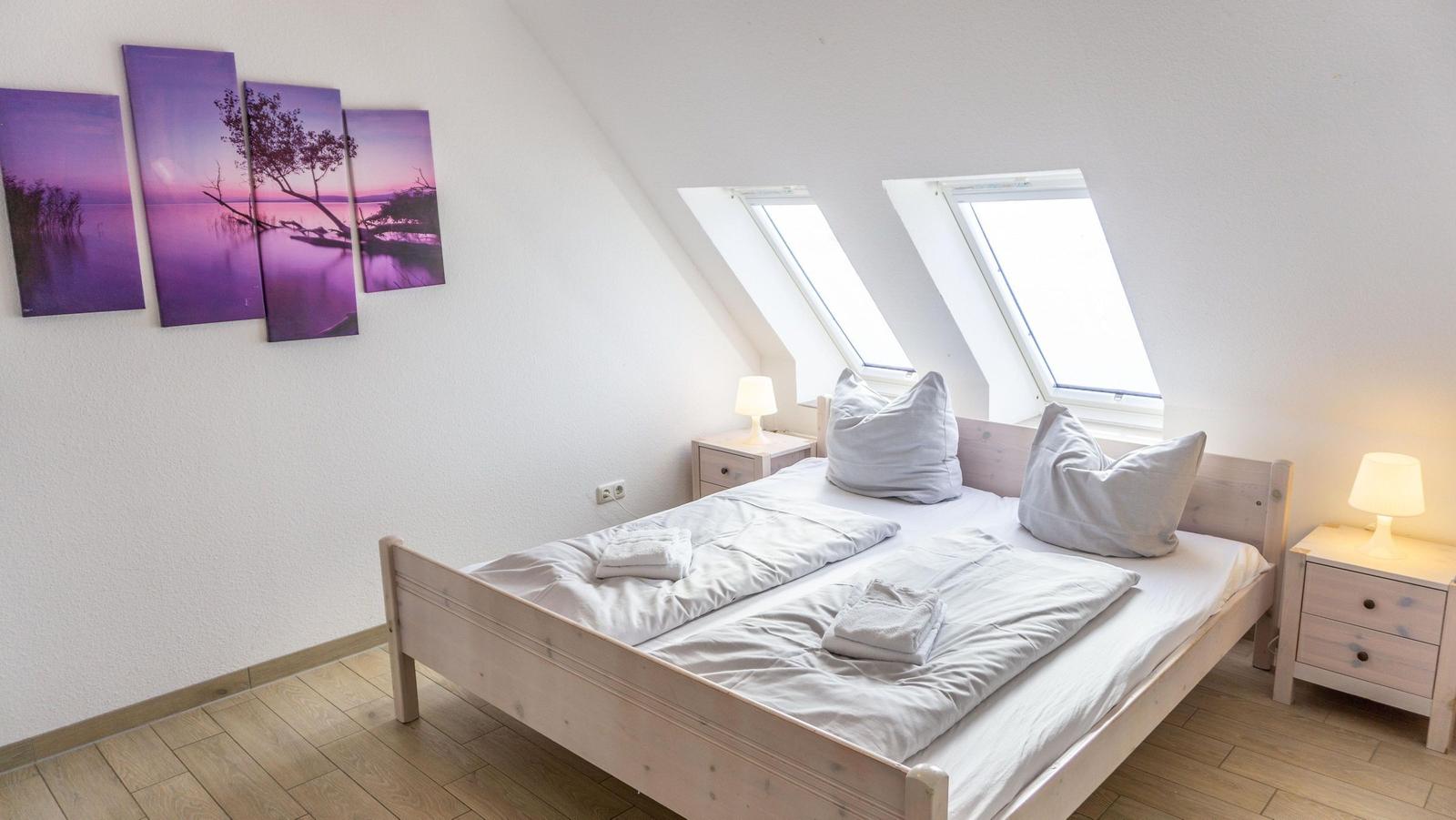 Schlafzimmer mit Dachschrägen, Doppelfenster und Wandbildern.