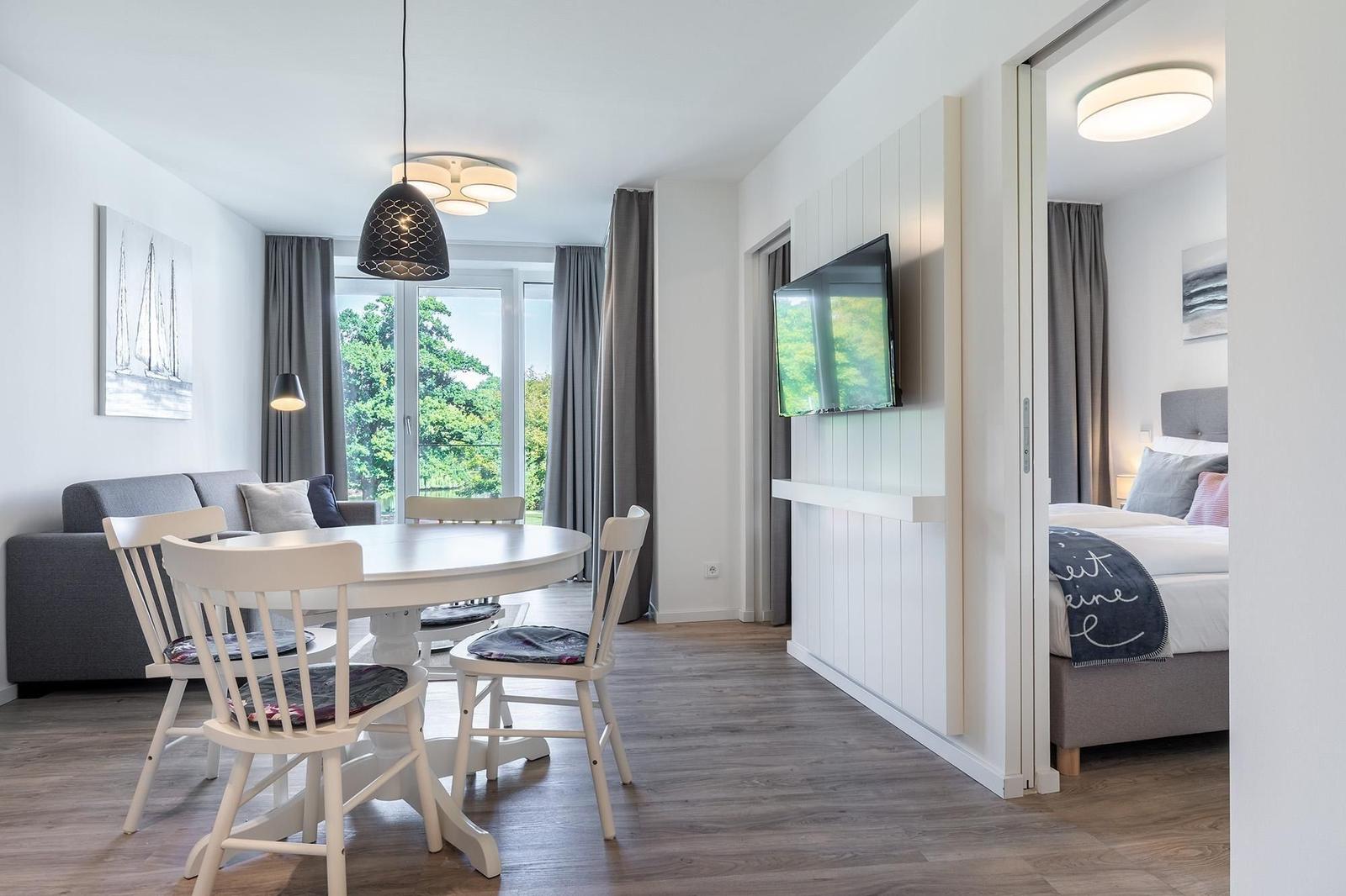 Wohnbereich mit Esstisch, Sofa und TV. Schlafzimmer mit Bett und Fenster sichtbar.