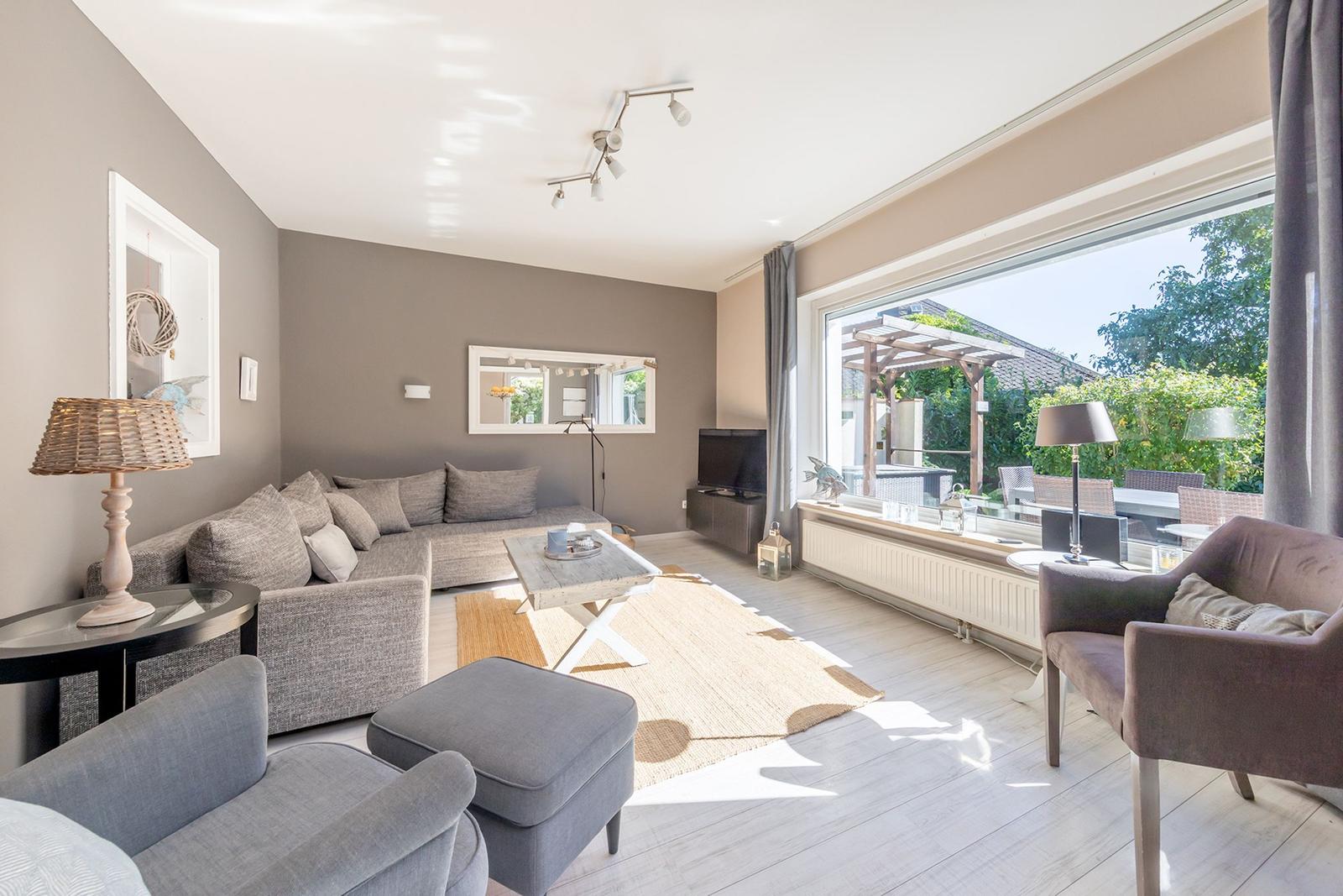 Wohnzimmer mit Sofa, Sessel und großem Fenster zur Terrasse.