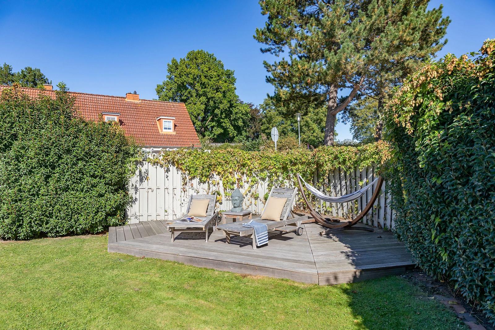 Hinterhof mit Holzterrasse, Liegen, Hängematte und Buddha-Statue.