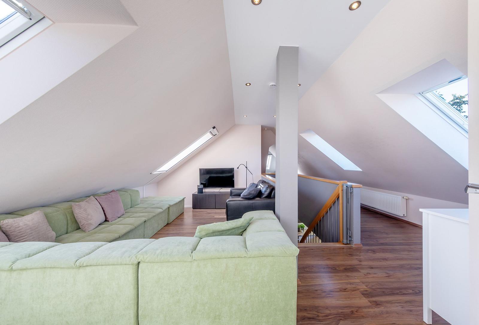 Wohnzimmer mit grünem Sofa, Holzboden und Dachschrägen mit Dachfenstern.