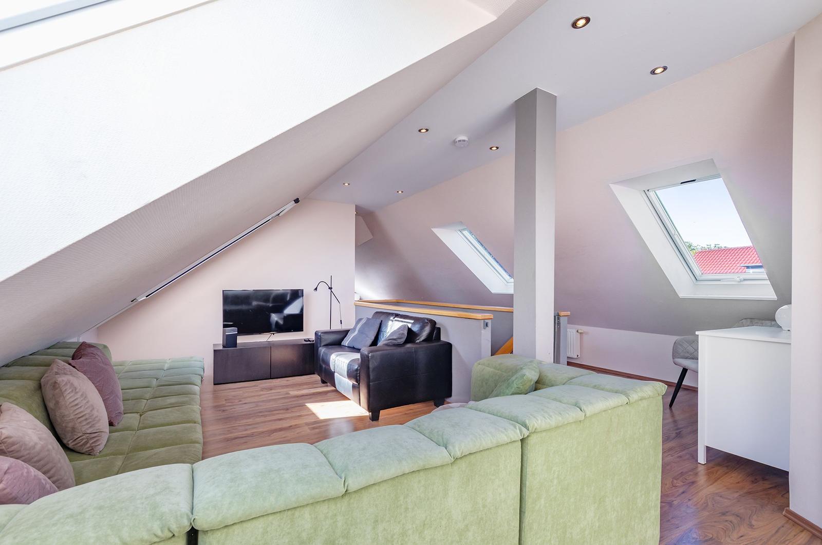 Dachgeschosswohnung mit grünem Sofa, Fernseher und Dachfenstern.