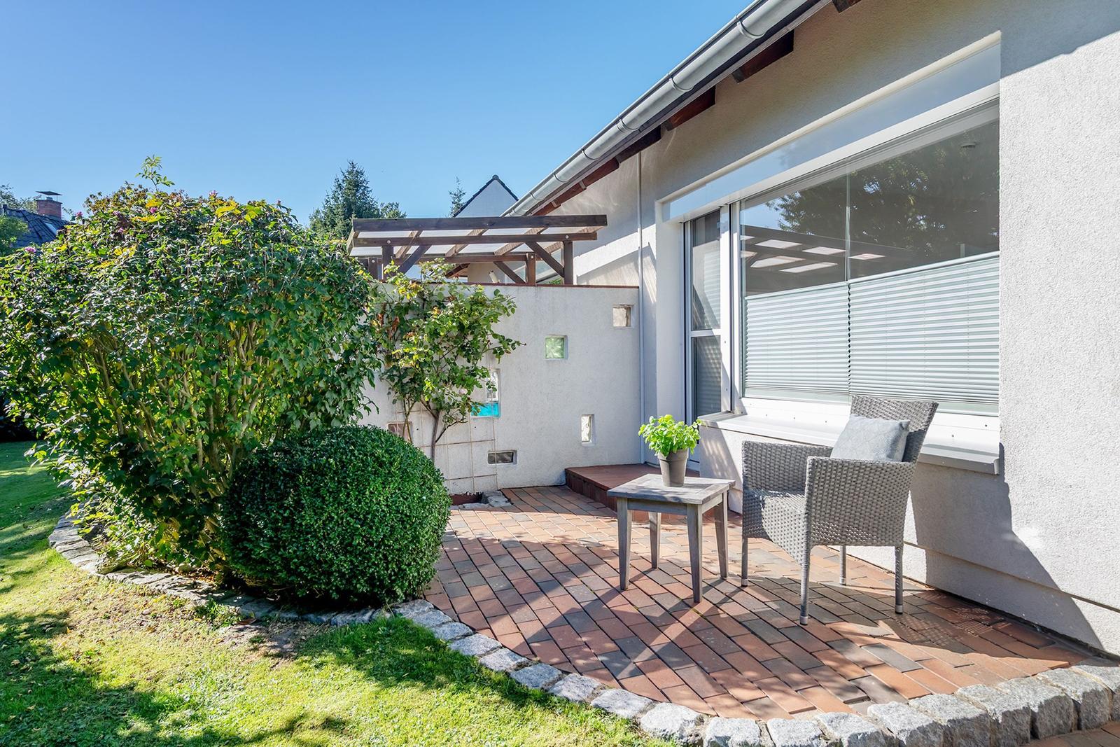 Terrasse mit Garten, Tisch und zwei Stühlen. Hinterhof mit Pergola und Beerensträuchern.