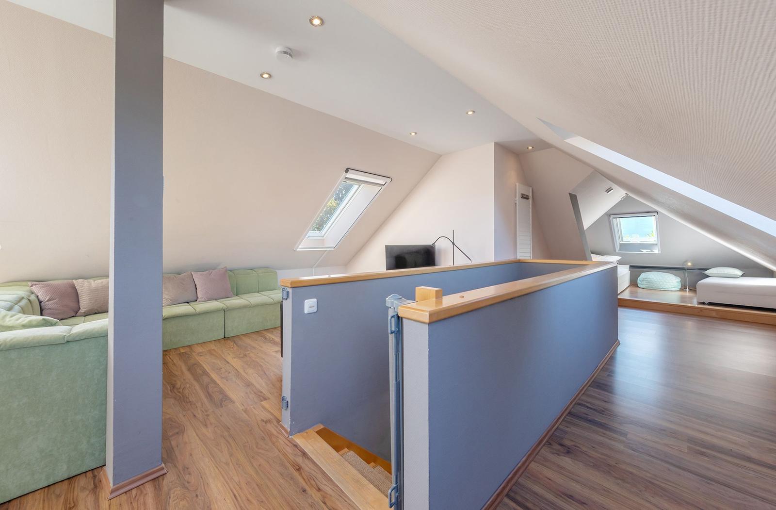 Dachgeschosswohnung mit Sofa, Bett und Dachfenstern.