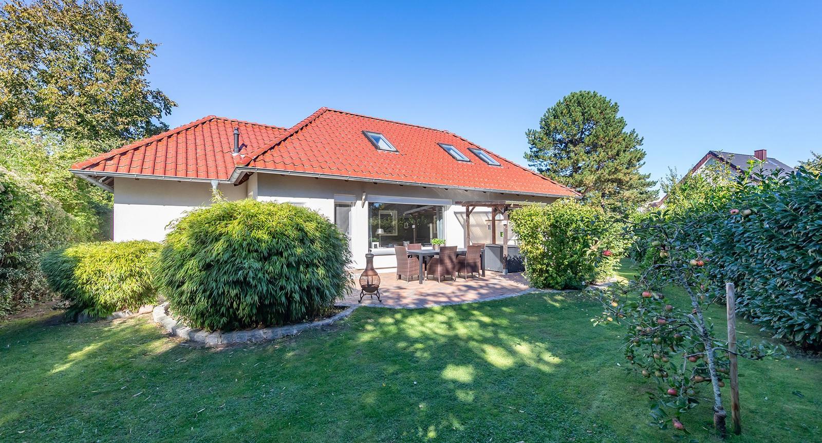 Haus mit rotem Dach, Terrasse und Garten mit Obstbaum.