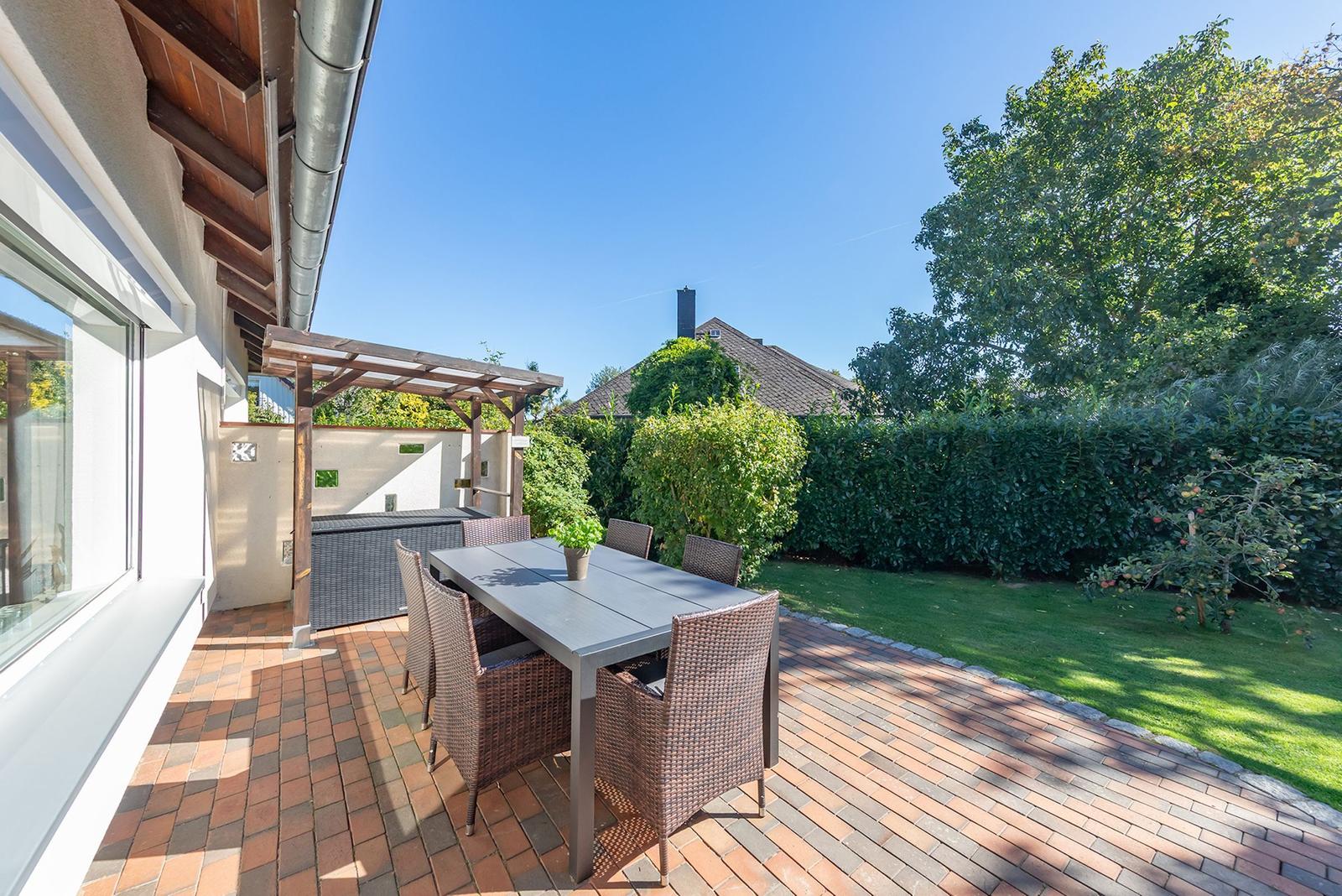 Terrasse mit Tisch, Stühlen und Pavillon. Grünflächen und Hecke im Hintergrund.
