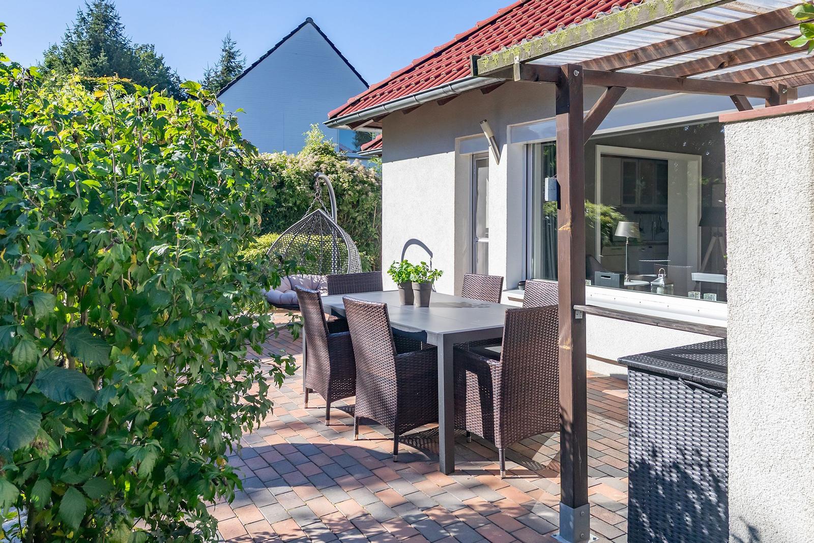 Terrasse mit Tisch, Stühlen und Hängesessel. Blick in die Küche.