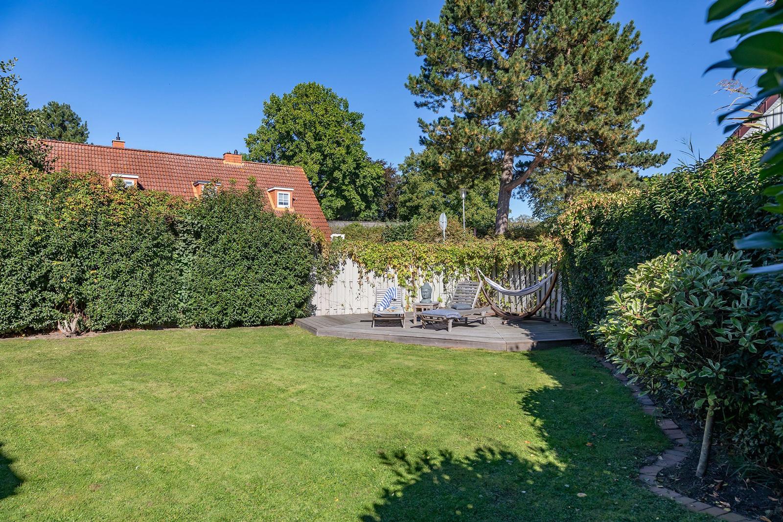 Hinterhof mit Terrasse, Liegestühlen und Hängematten umgeben von Grünflächen und Bäumen.