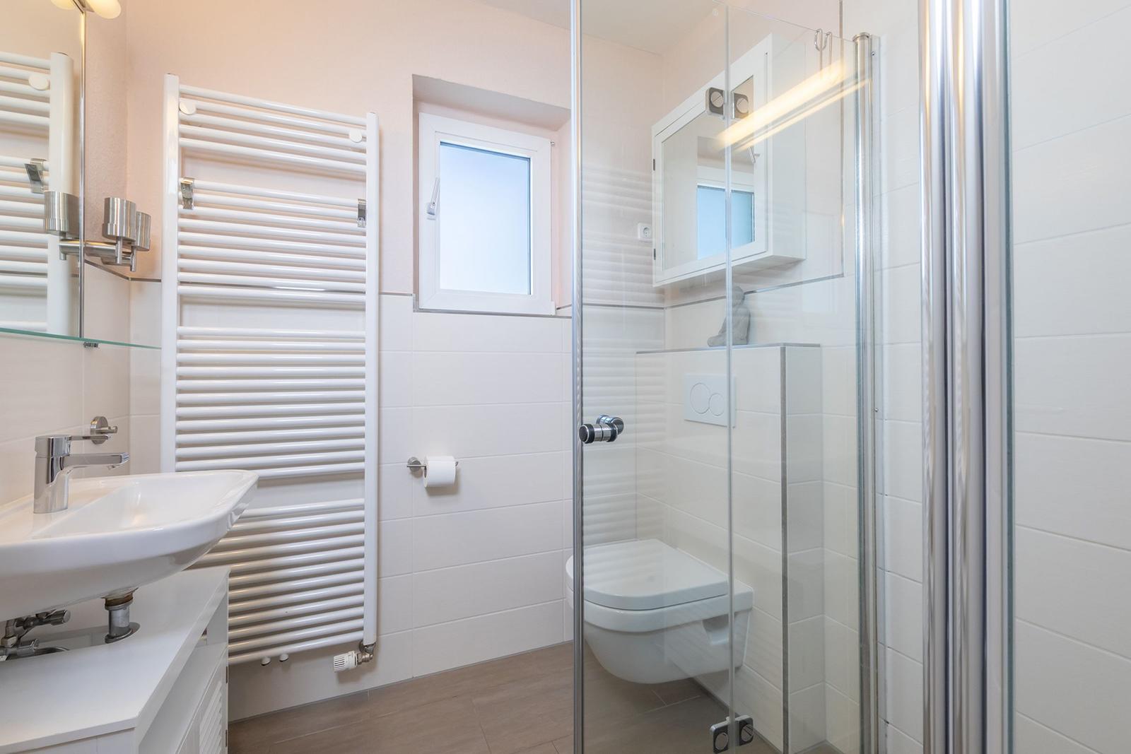 Badezimmer mit Dusche, Toilette, Waschbecken und Heizung.