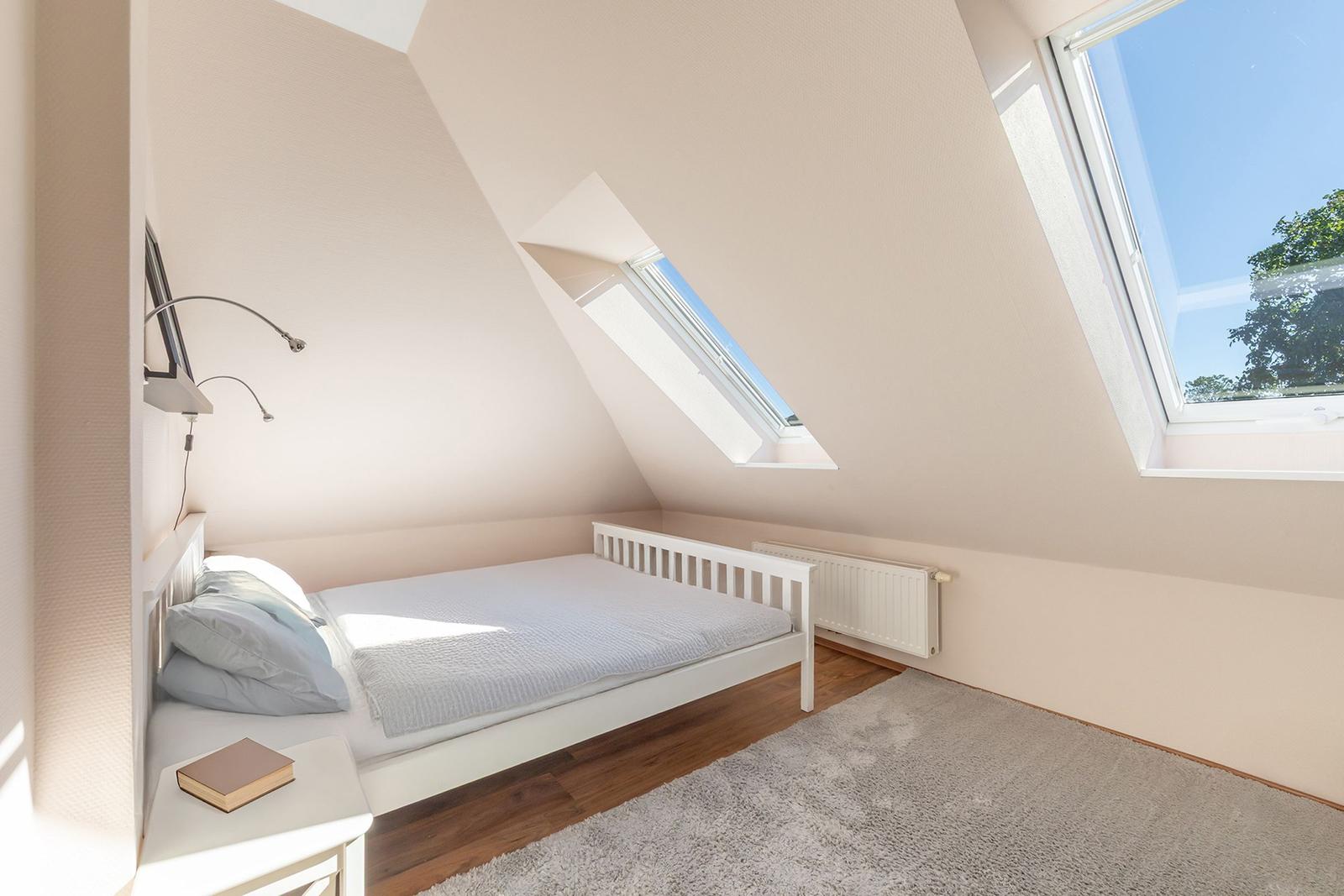 Schlafzimmer mit Dachschrägen, Bett, Fenster und Teppichboden.